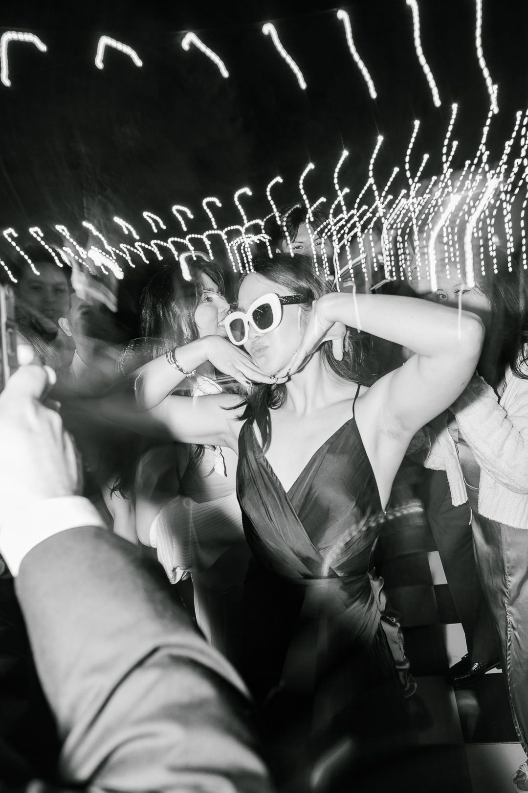 Long exposure black and white photo of people dancing in a nightclub creates blurred motion trails.