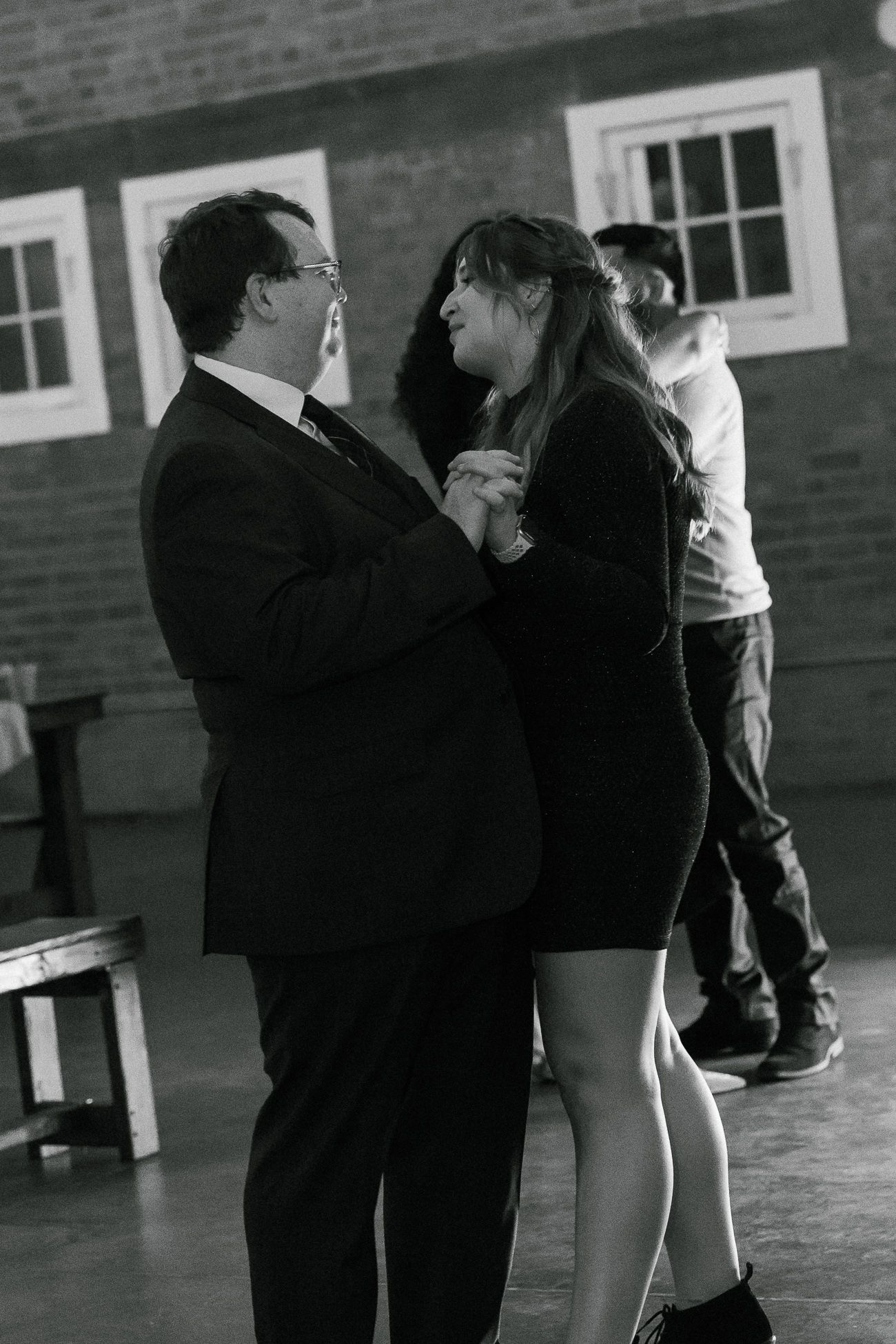 Two people dance together in formal attire at an indoor venue with brick walls.