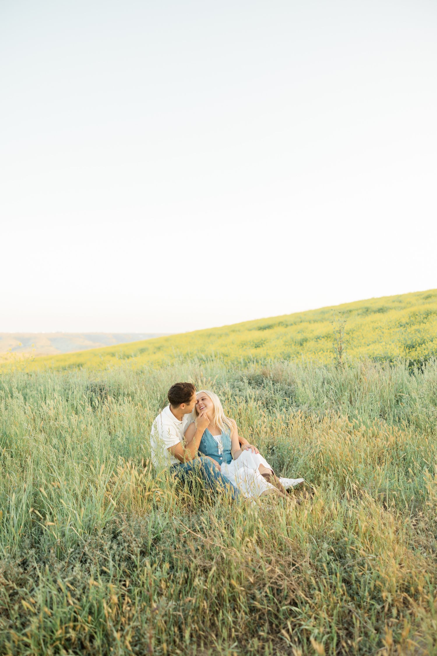 Couple lying in a grassy meadow during golden hour, sharing an intimate moment in nature.