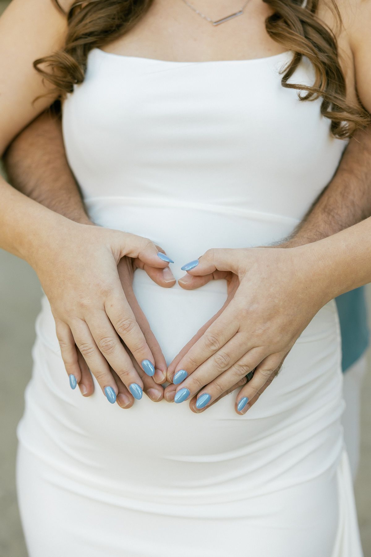 Series of hands forming a heart shape on a white dress showing pregnancy progression over time.