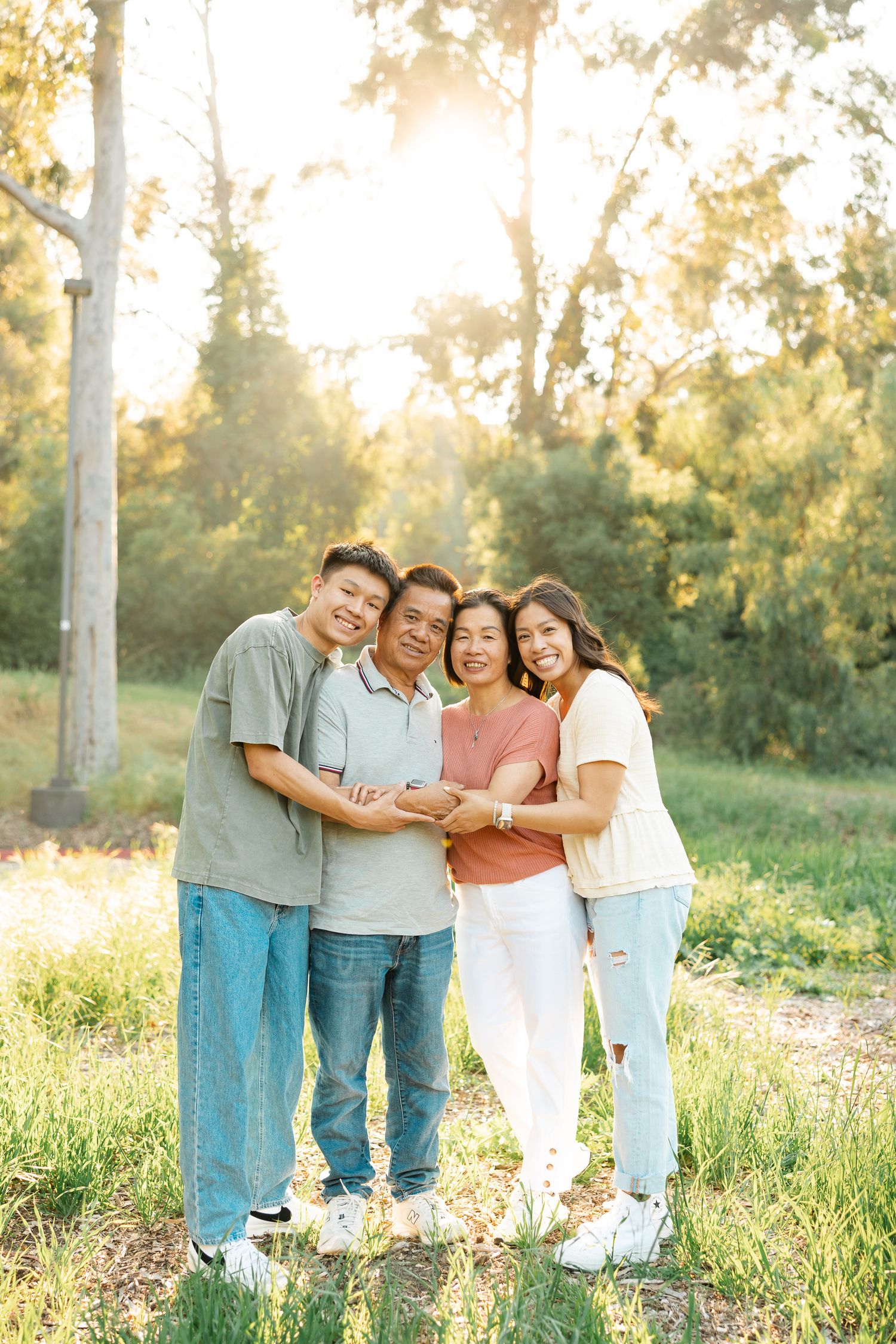 Family members embrace while standing in a sunlit meadow with eucalyptus trees behind them.