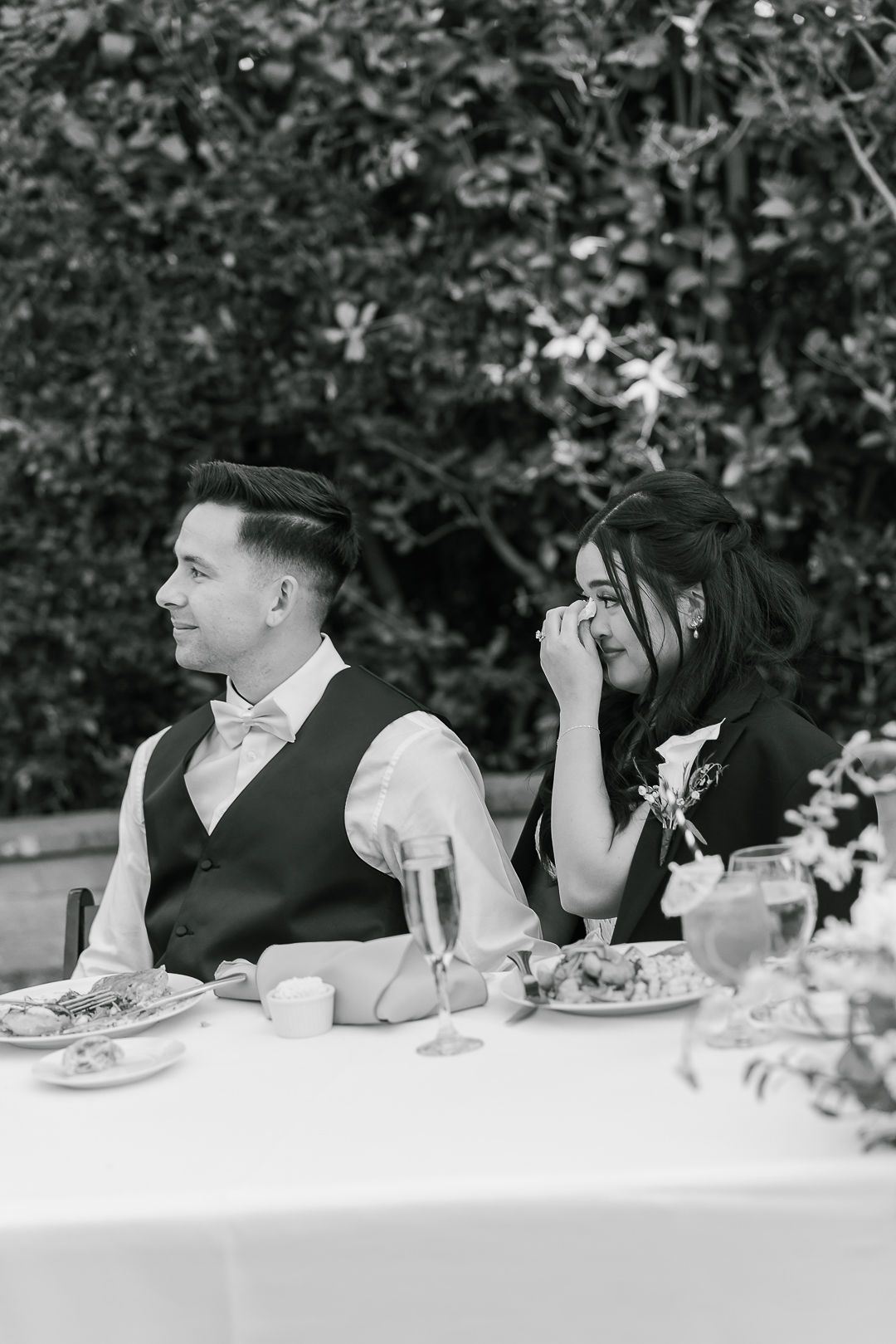 Black and white photo of two people dining at an elegant outdoor table setting with white linens and place settings.