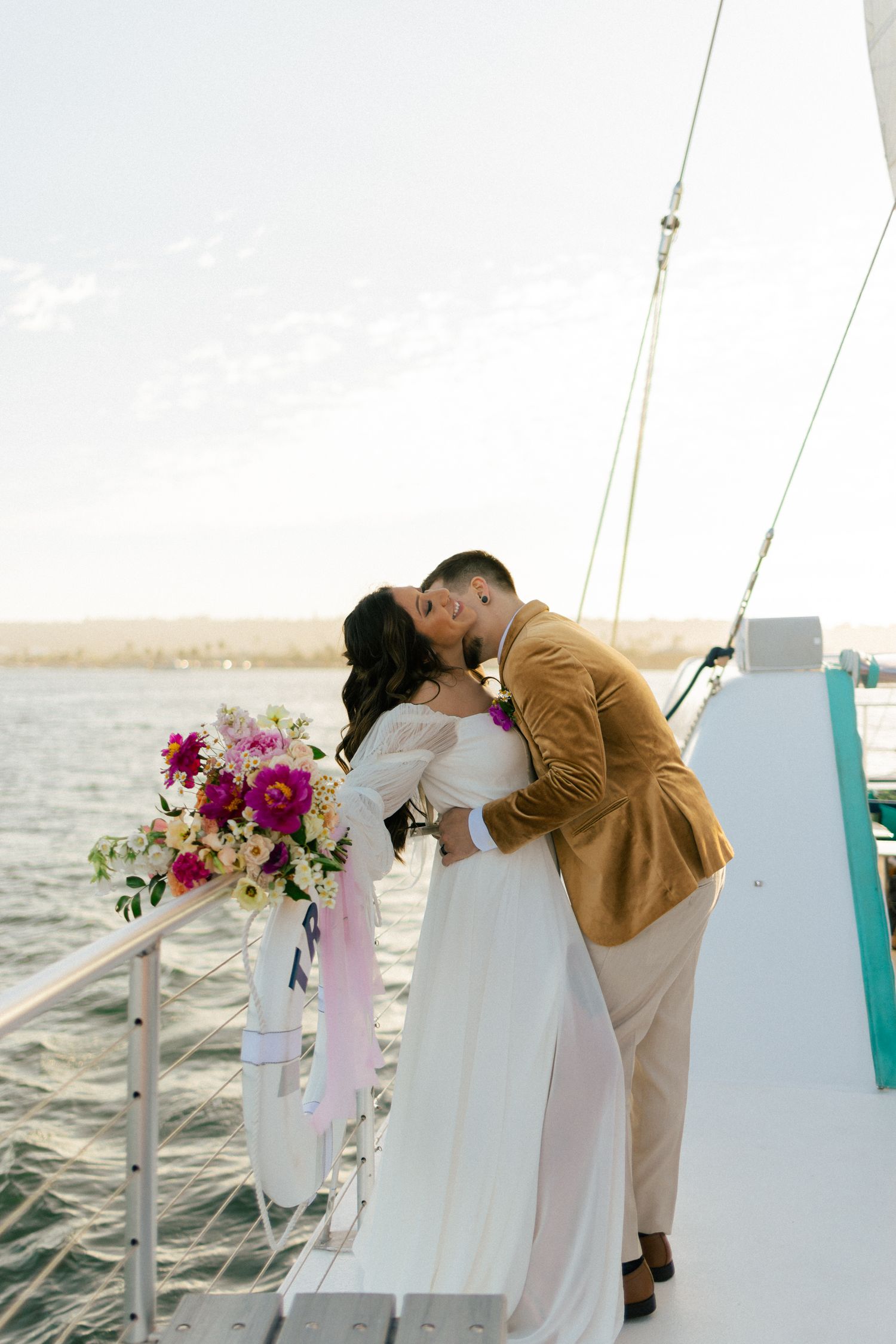 A couple shares a romantic kiss on a yacht deck with vibrant pink flowers nearby.