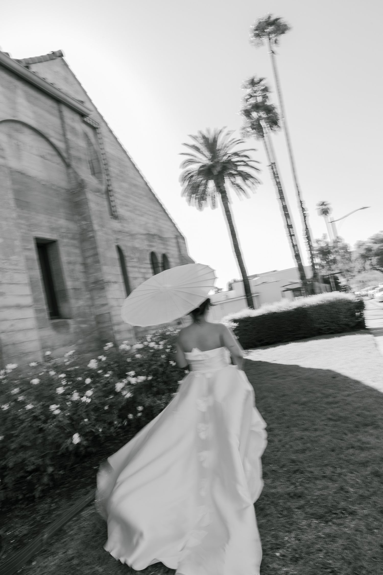 A figure in white holding a parasol twirls near a stone church with palm trees in the background.