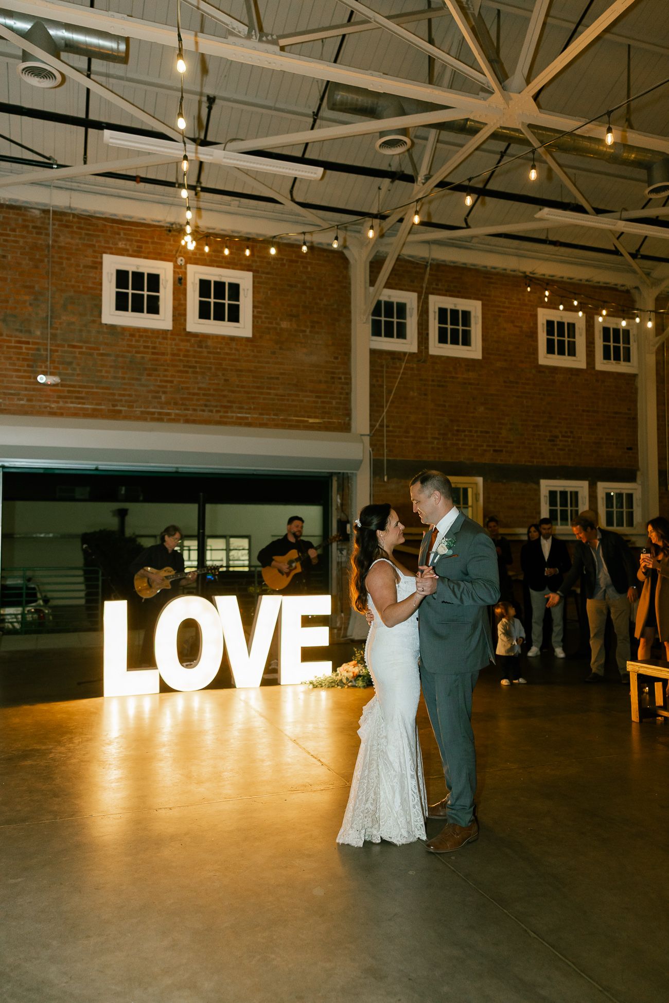 Wedding reception venue with illuminated LOVE sign and string lights hanging from industrial ceiling.