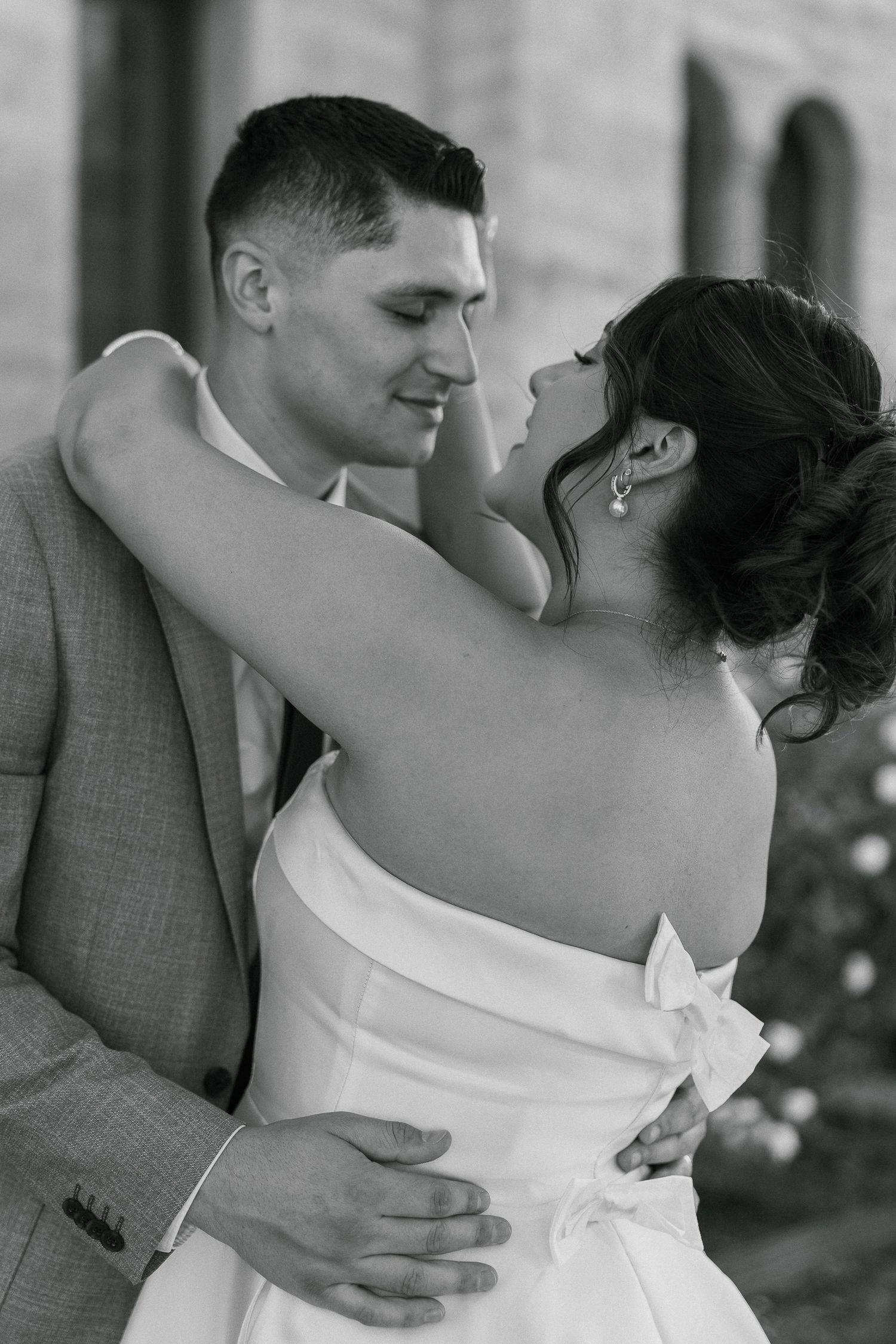 An intimate black and white portrait of a couple embracing in wedding attire with the bride in a strapless gown.