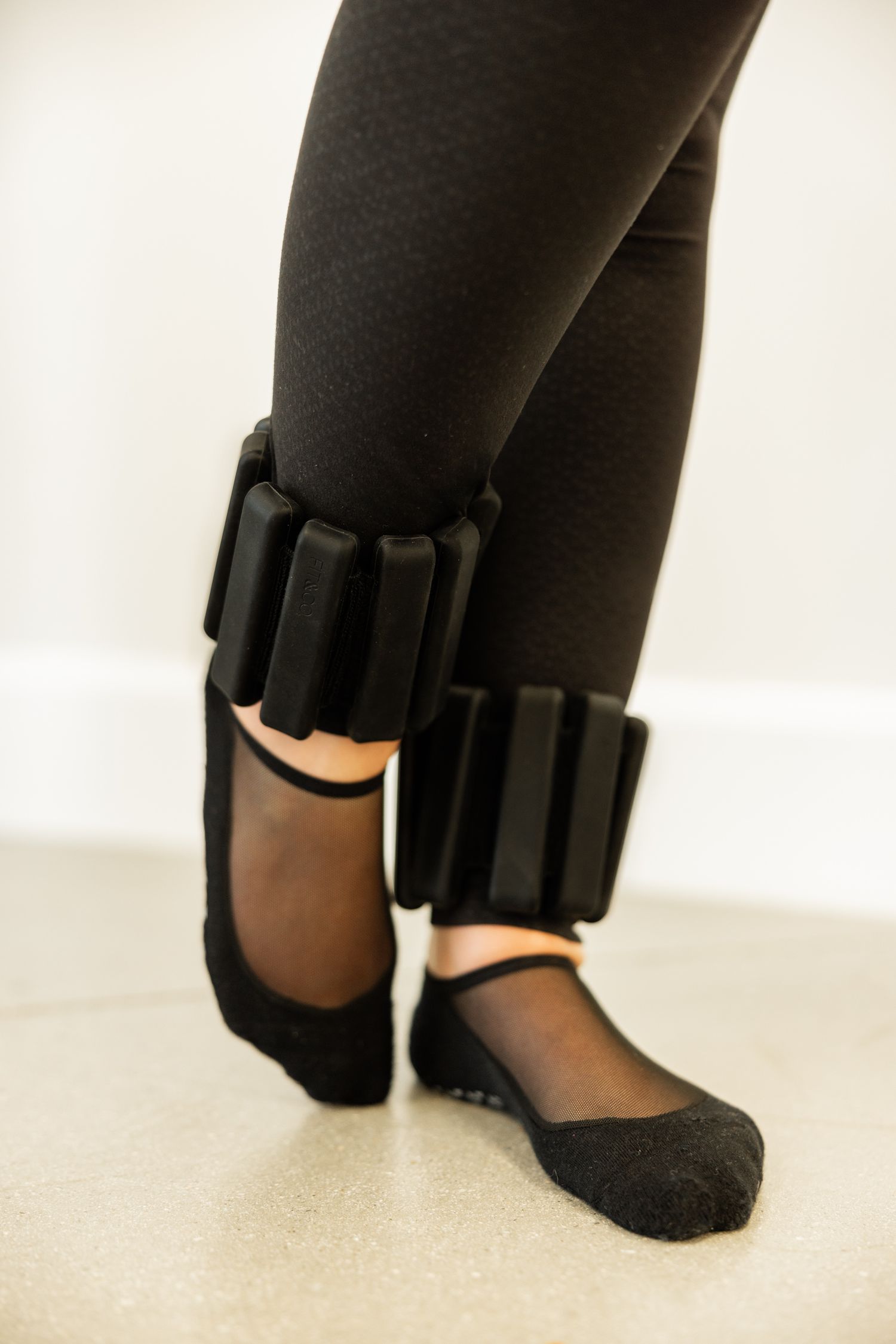 Close-up view of legs wearing black ankle weights during exercise or physical therapy.