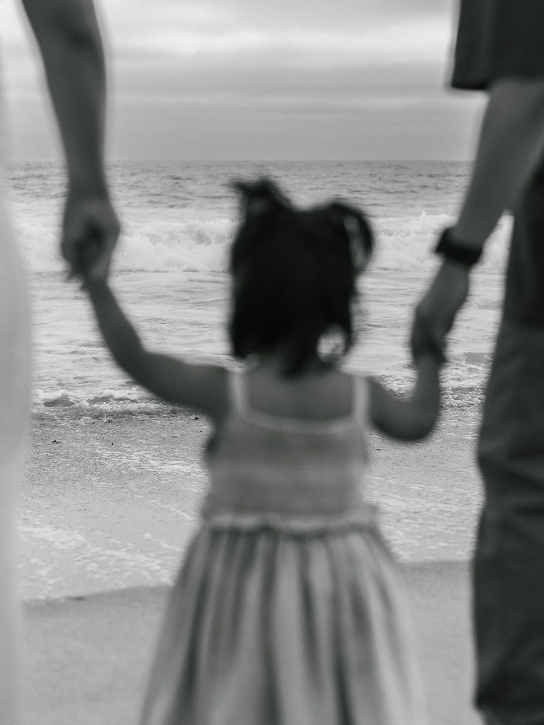 A black and white motion-blurred photo shows a person in a dress twirling on a beach with ocean waves in background.