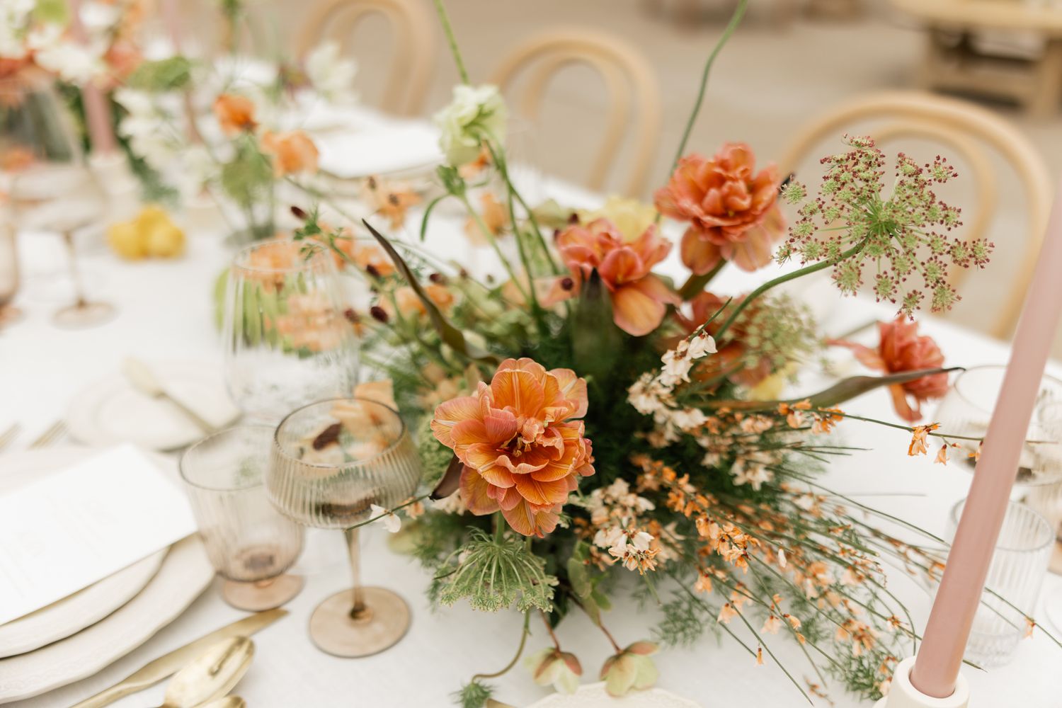 Elegant floral centerpiece with coral poppies and delicate white flowers on a wedding reception table setting.
