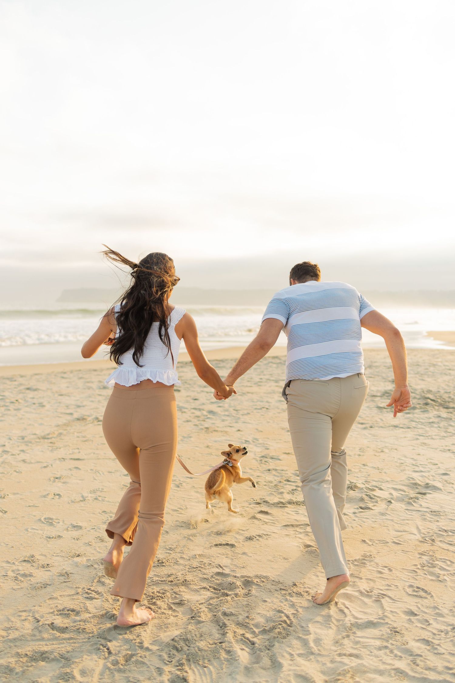 A couple runs playfully together on a sandy beach at sunset, creating joyful footprints in their wake.