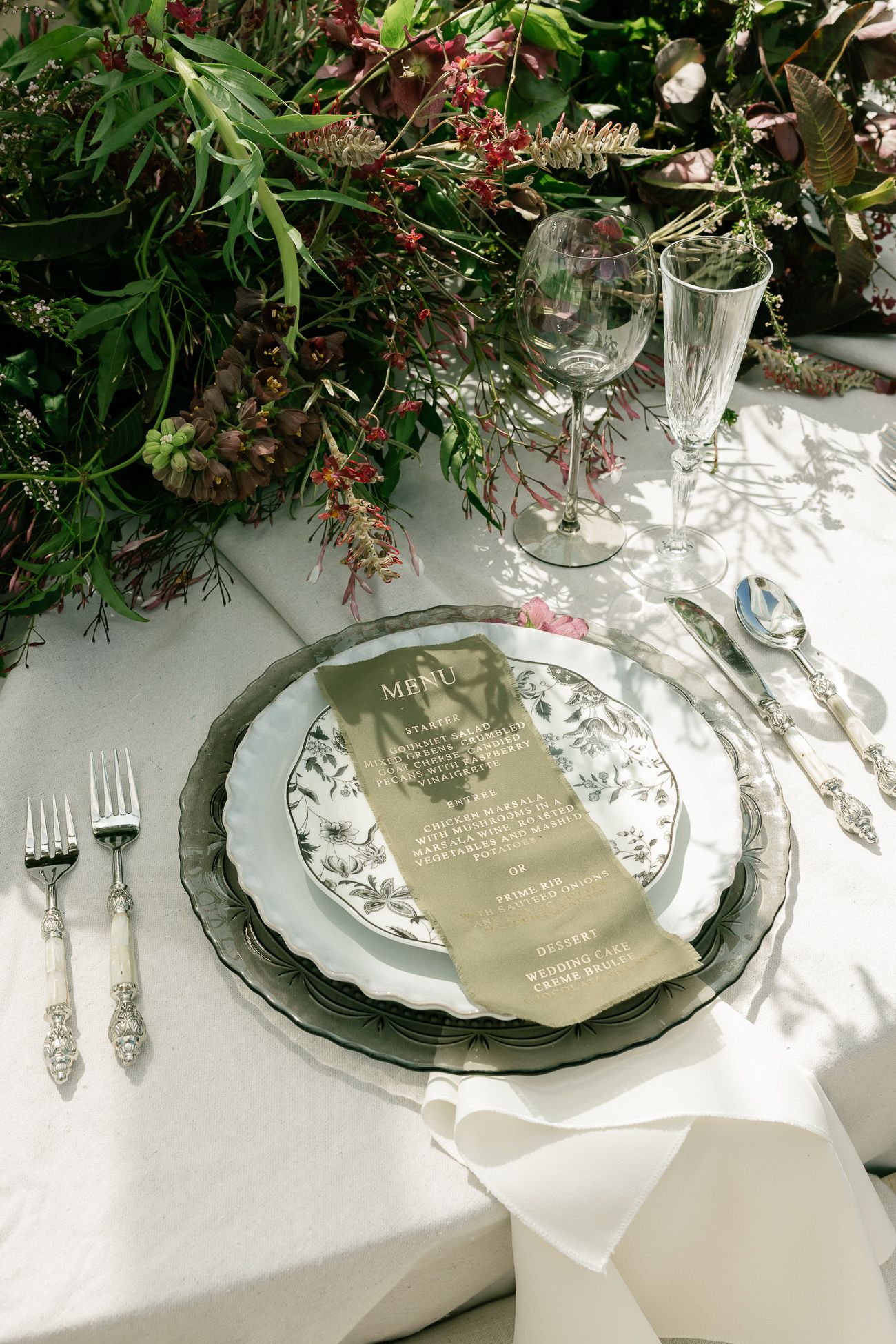 Elegant holiday table settings with white plates, silver cutlery, and fresh greenery garland decorations.
