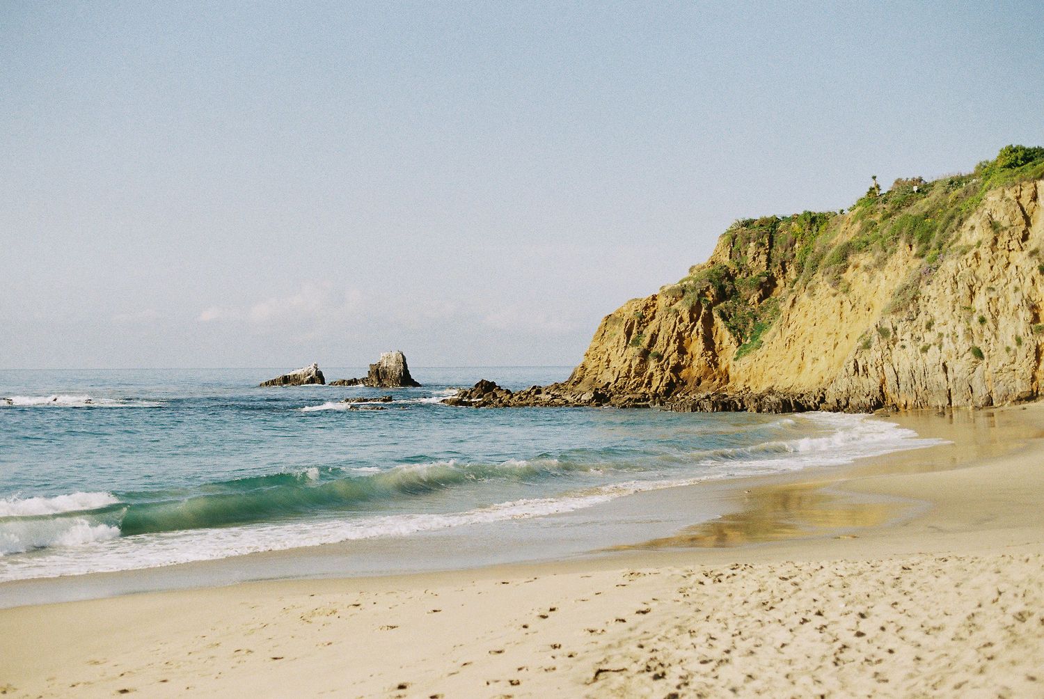 Scenic coastal panorama showing rugged cliffs and sandy beaches along a turquoise ocean shoreline on a sunny day.