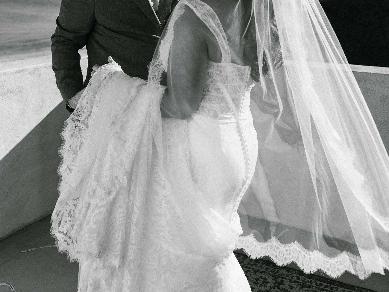 A black and white photo showing the detailed lace and veil of a wedding dress from behind.