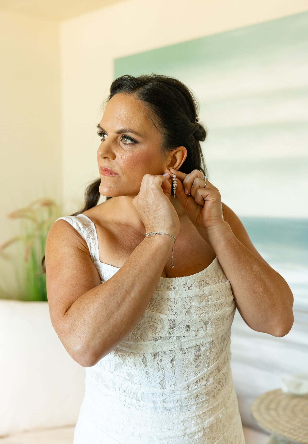 Person in white lace bridal gown puts on earrings while getting ready.