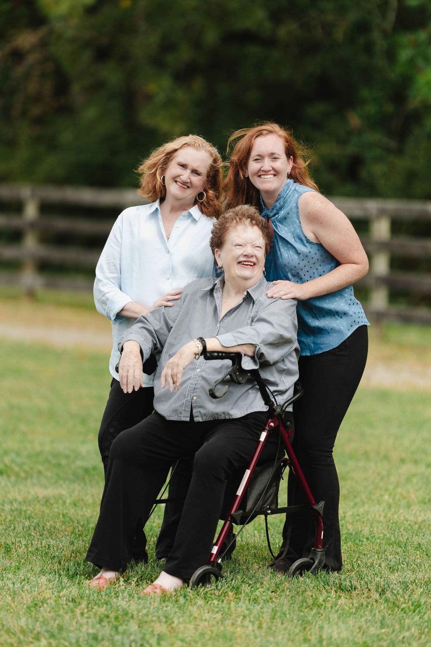 Three people pose together smiling outdoors on grass.