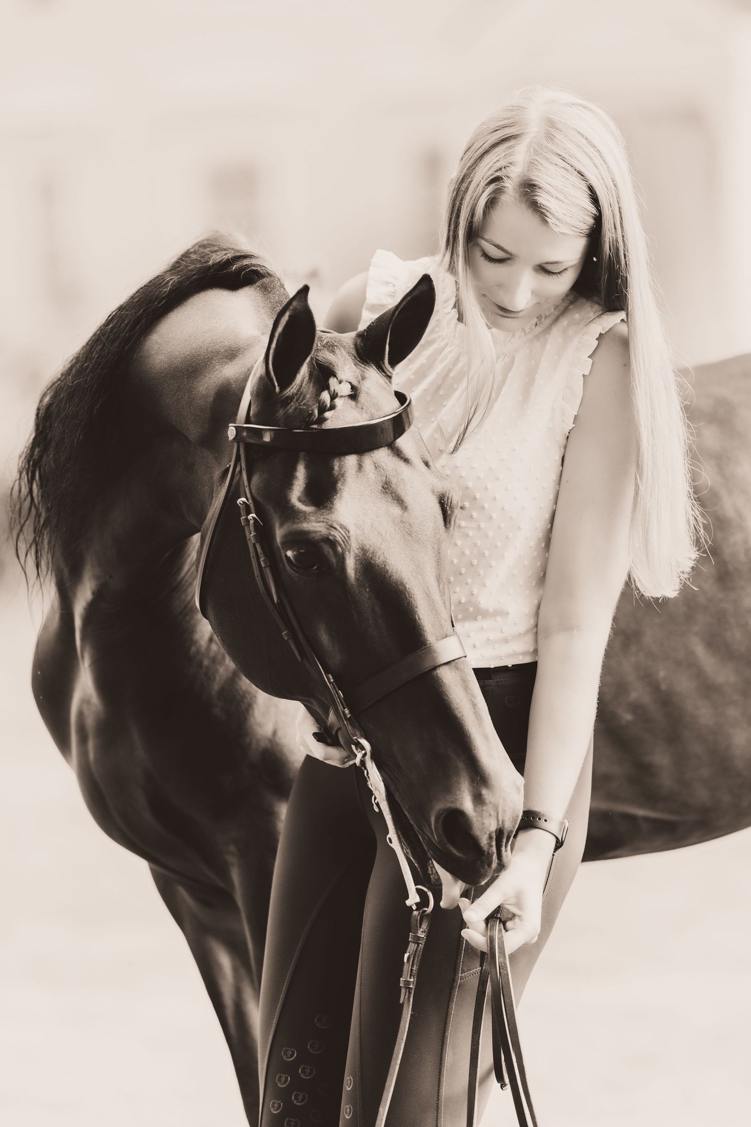 A sepia-toned photograph shows a woman in a white top standing with a dark-colored horse against a soft background.