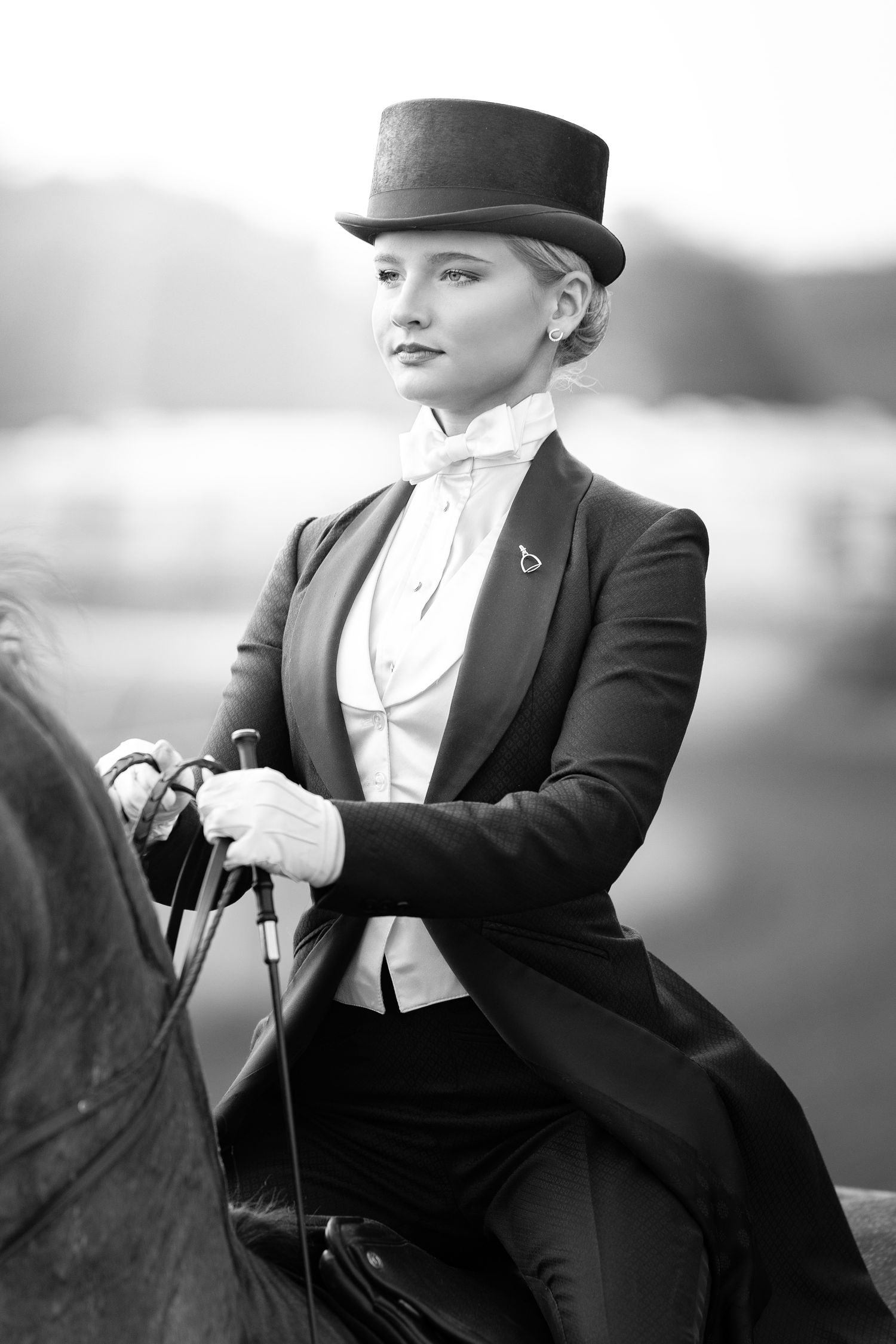 Elegant equestrian rider in formal attire with top hat and tailcoat sitting sidesaddle in black and white photograph.
