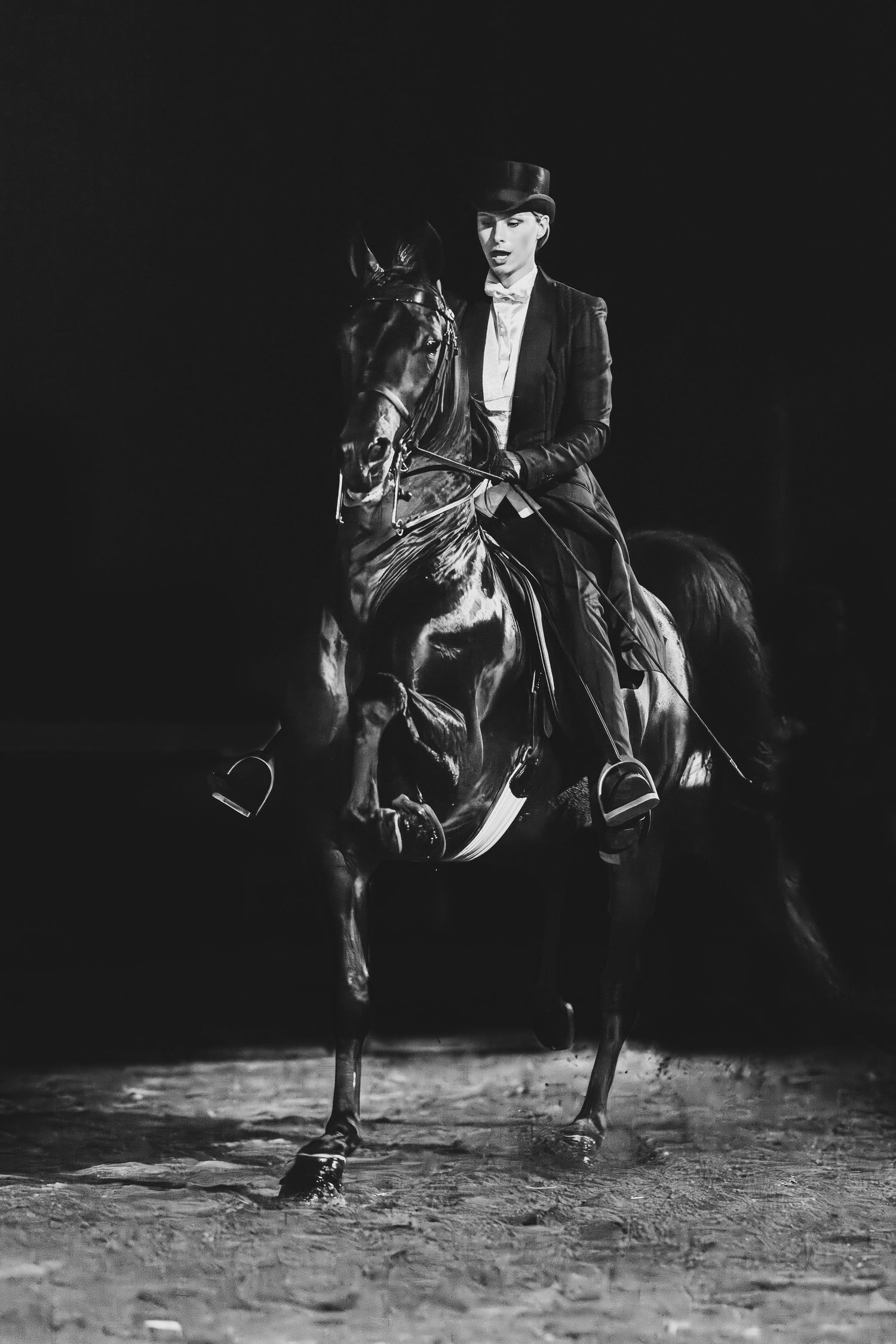 A black and white vintage photograph of an equestrian in formal attire riding a dark horse against a dark background.