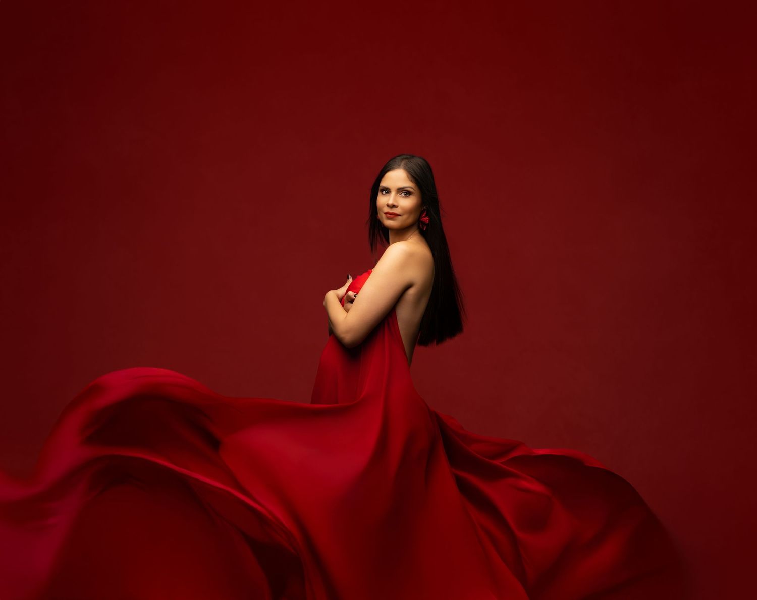 A flowing red dress billows dramatically against a deep burgundy background creating an elegant artistic composition.