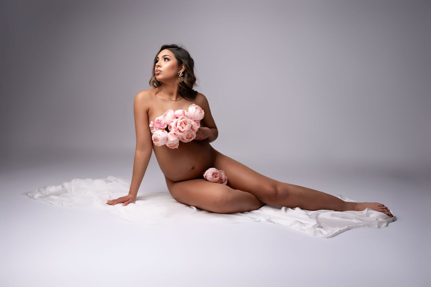 Artistic boudoir photo featuring pink roses against white fabric in a professional studio setting.