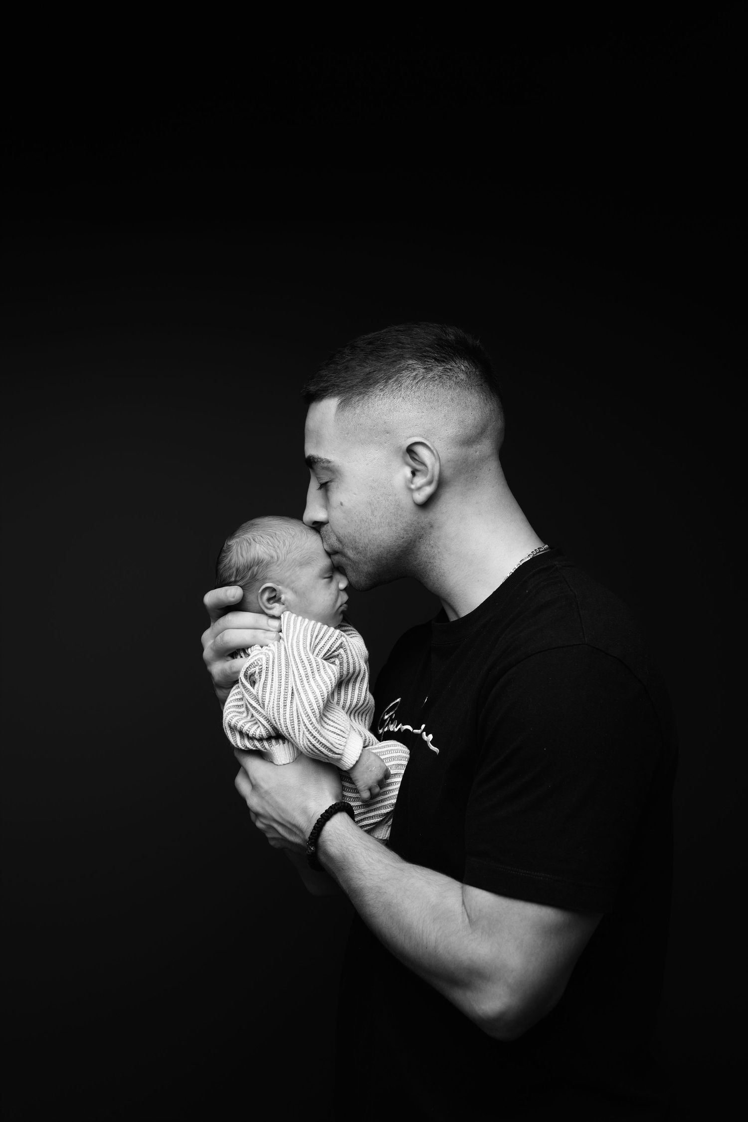 A series of black and white photos showing tender moments between a parent and infant in silhouette against dark background.