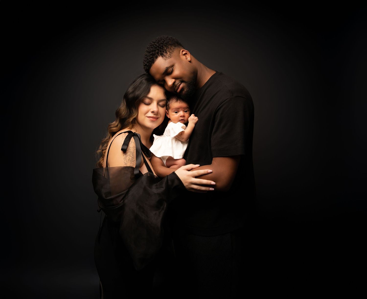 A couple embraces intimately against a dark background in a dramatic black and white portrait.