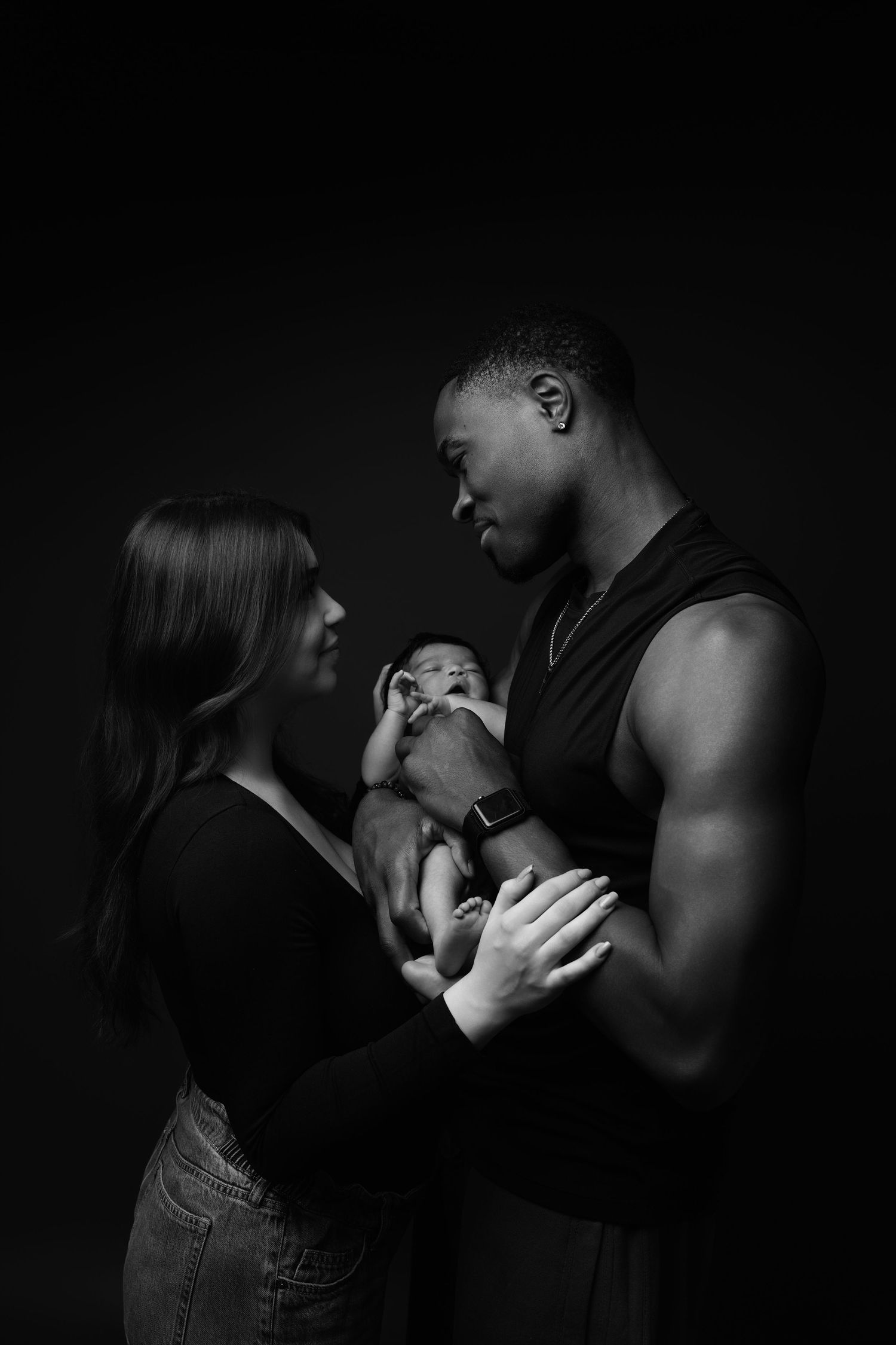 Black and white portrait of a couple holding a small puppy between them against a dark background.