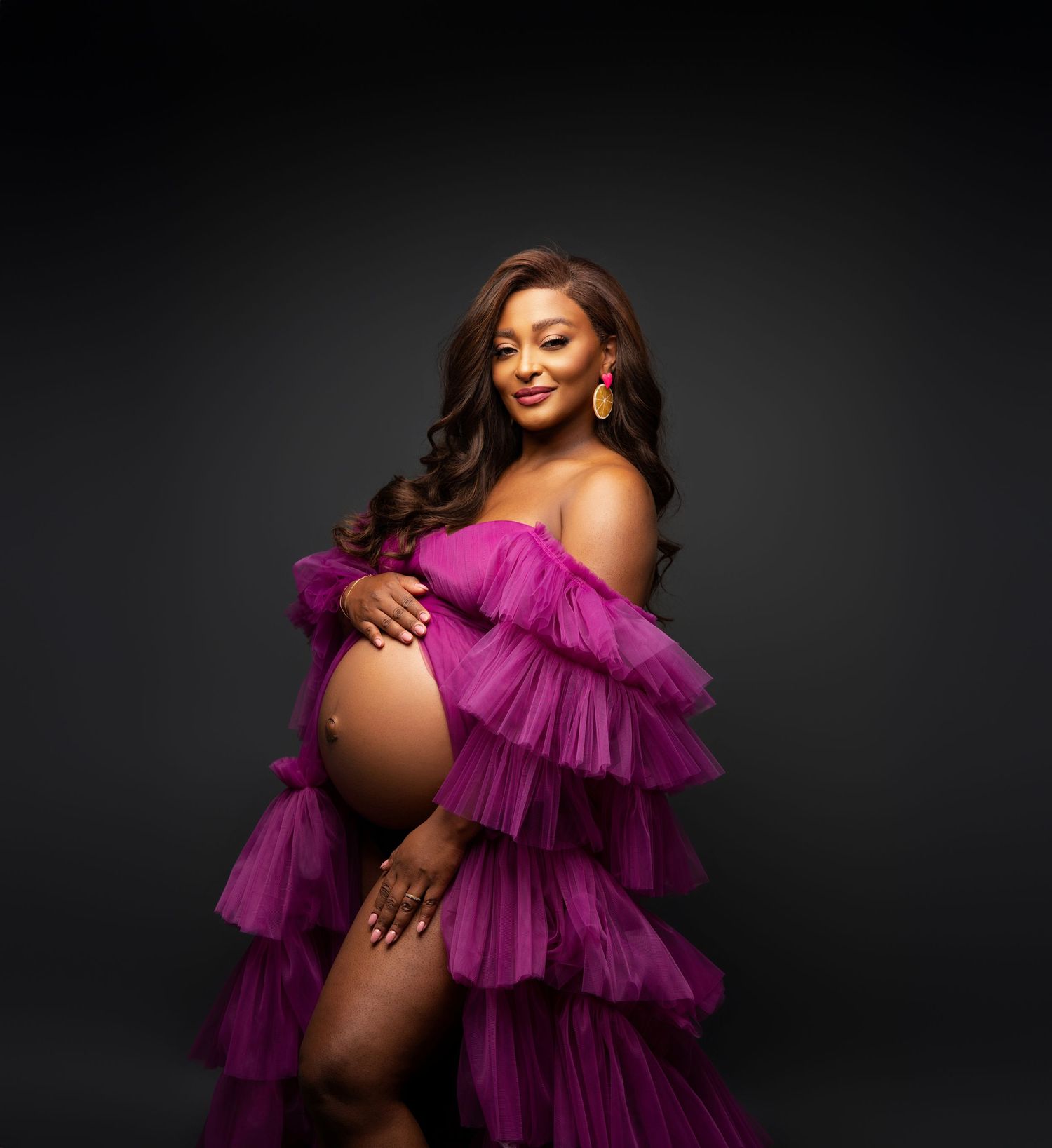 Maternity portrait of an expectant mother wearing a dramatic purple ruffled gown against a dark background.