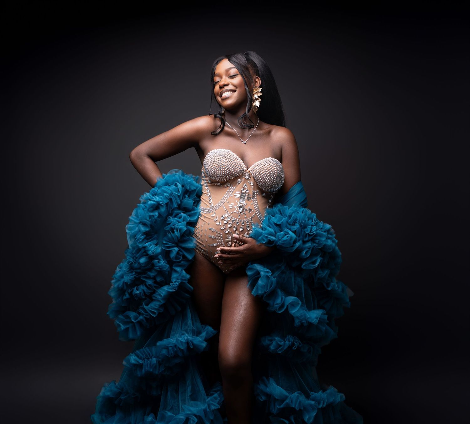 Portrait photoshoot in studio with dramatic lighting and flowing blue feathered boa against dark background.