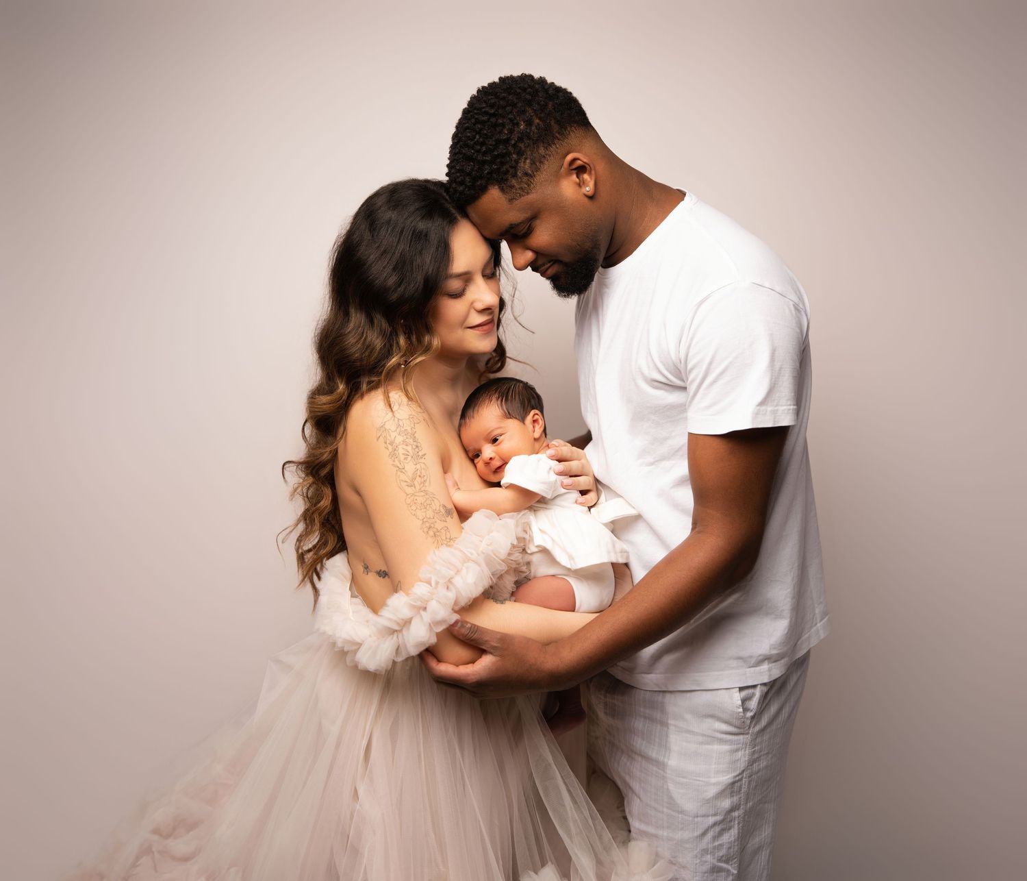 A family in white outfits shares tender moments together in a series of intimate studio portrait photographs.
