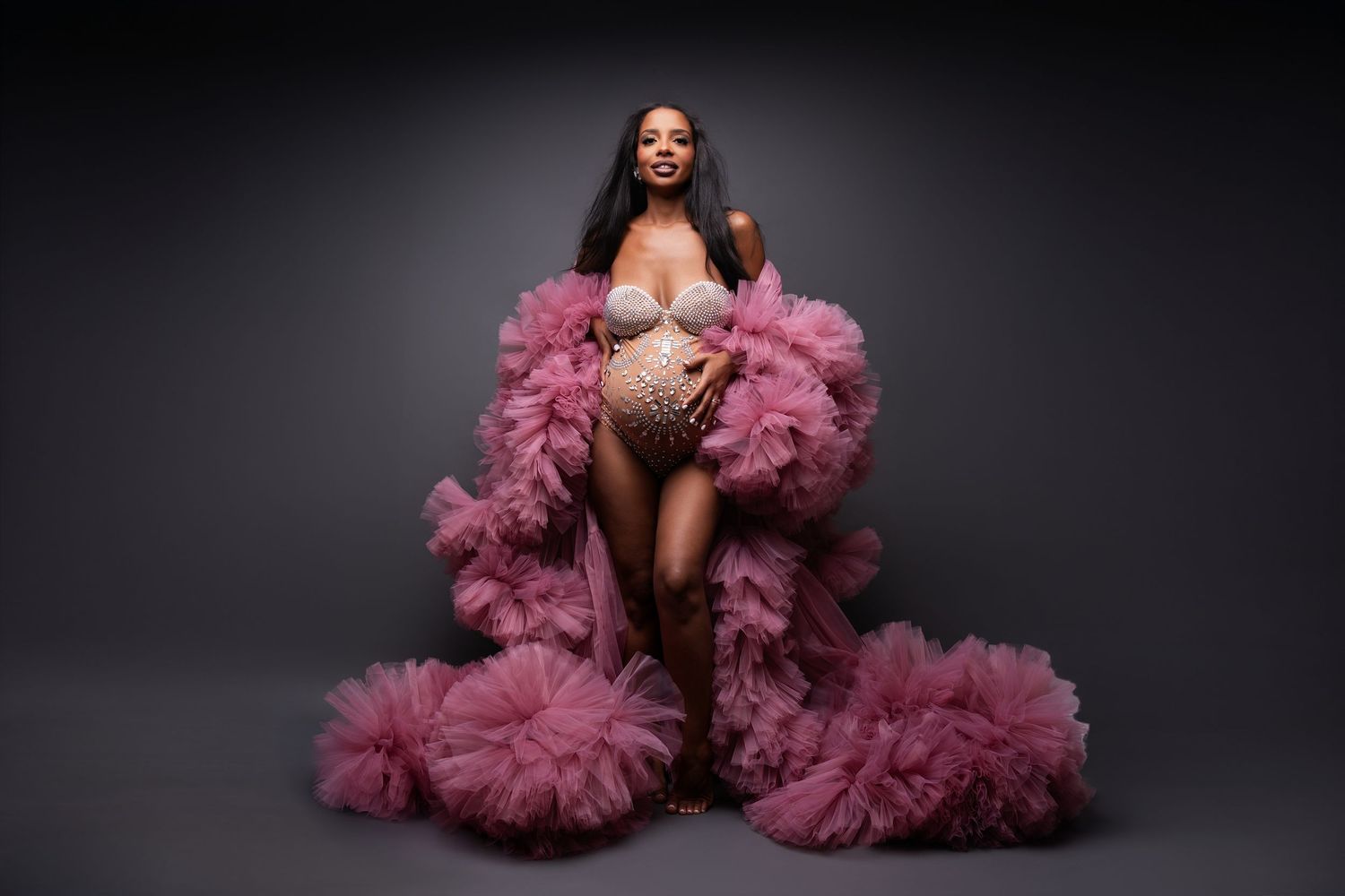 A model poses in a dramatic mauve tulle ruffled gown against a black backdrop in an artistic fashion photo series.