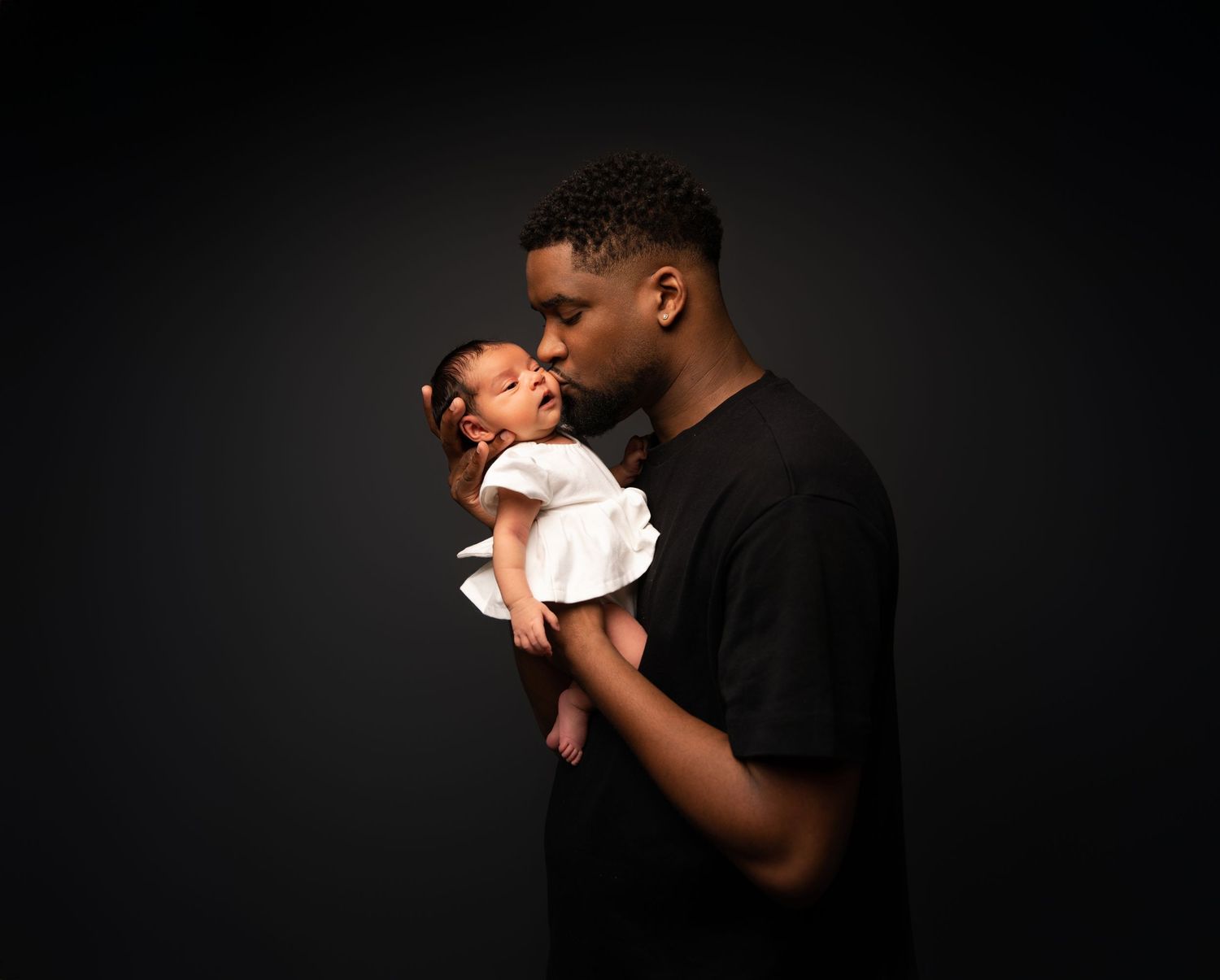 A tender black and white photo series showing a parent cradling and bonding with a newborn baby against a dark background.