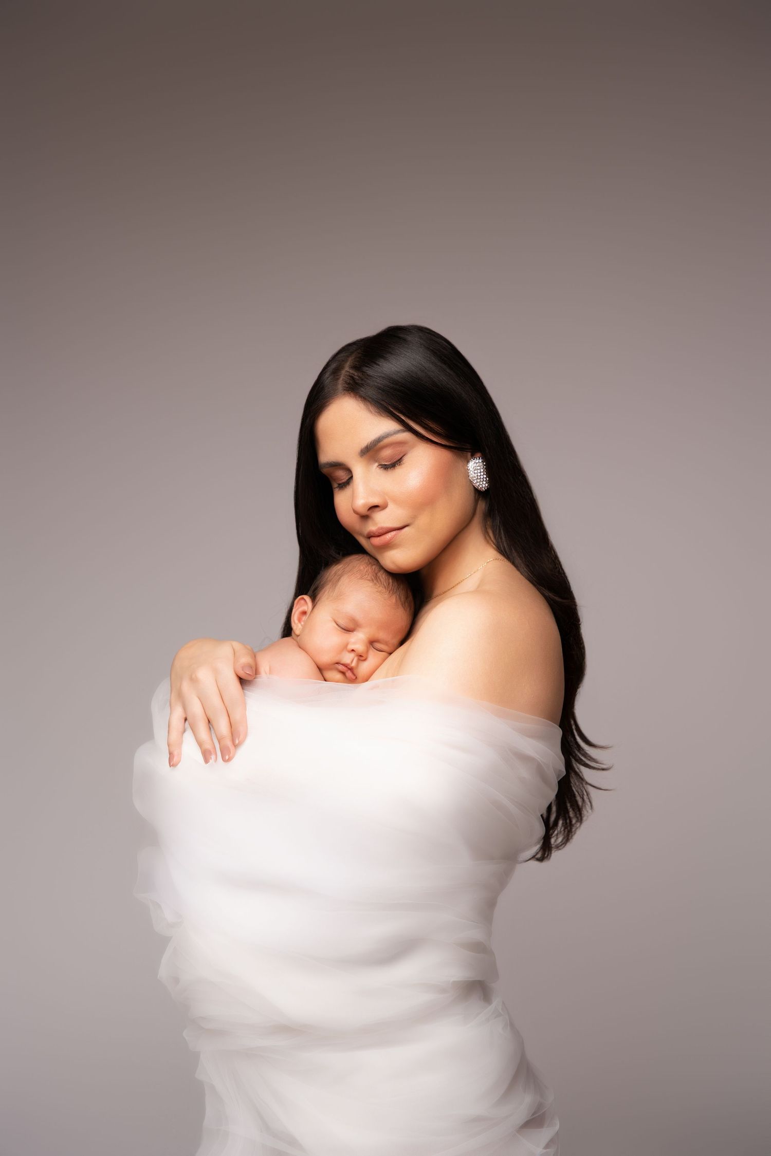 A tender portrait series showing a parent cradling a newborn baby wrapped in soft white fabric against a gray backdrop.