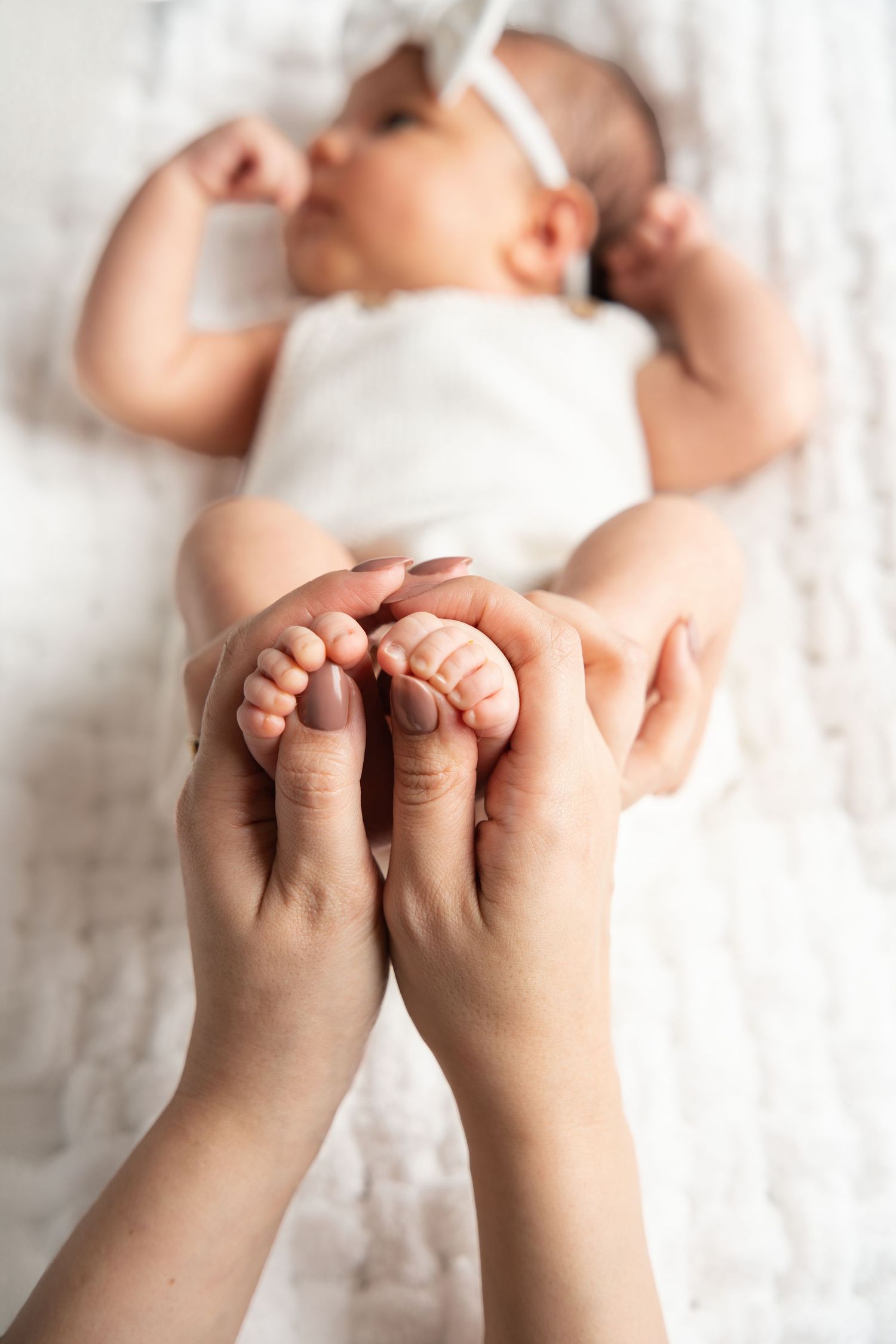 Close-up view of tiny baby feet being gently held by adult hands against white background.