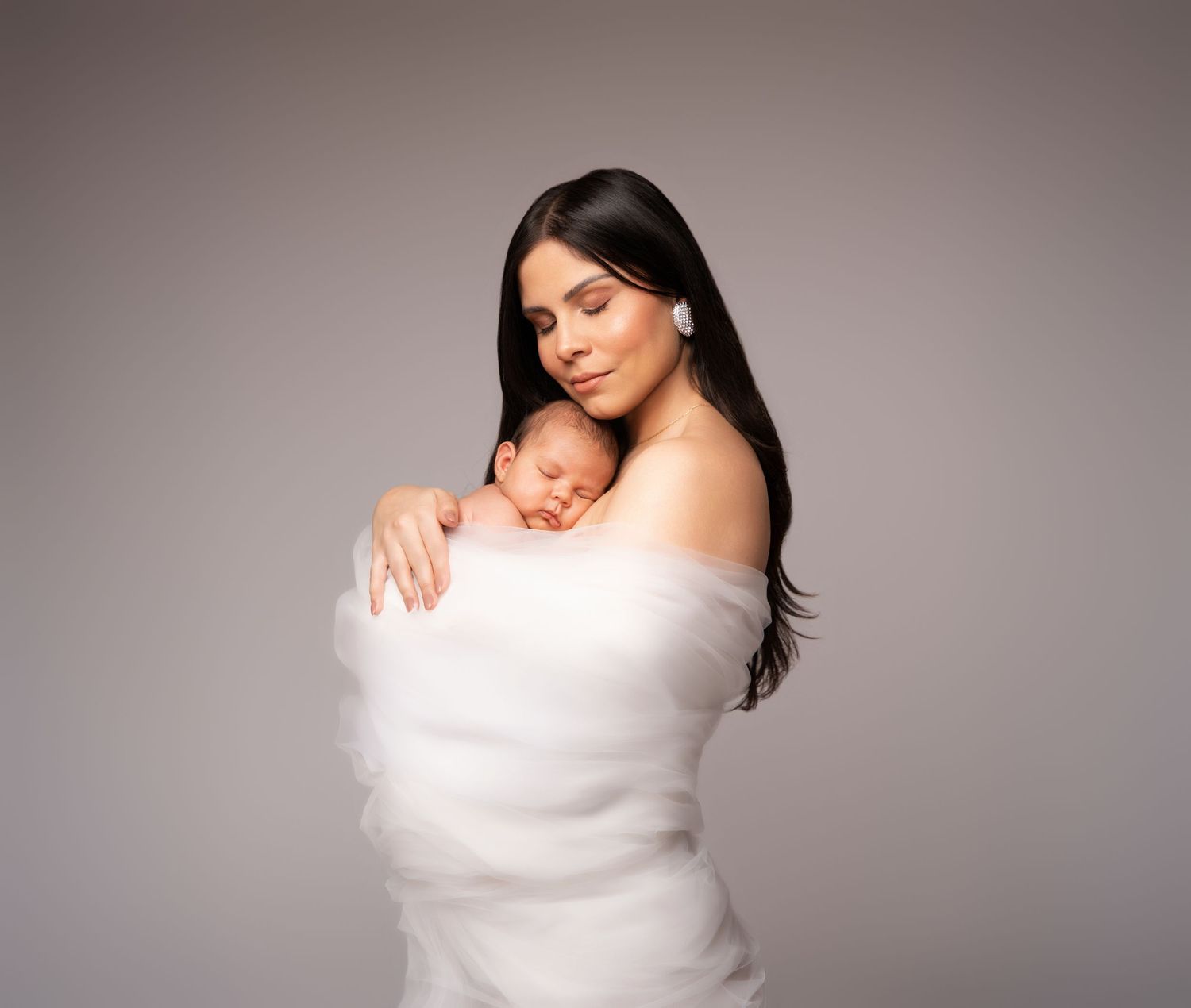 A tender moment captured as a sleeping newborn baby rests against someone wearing white fabric.