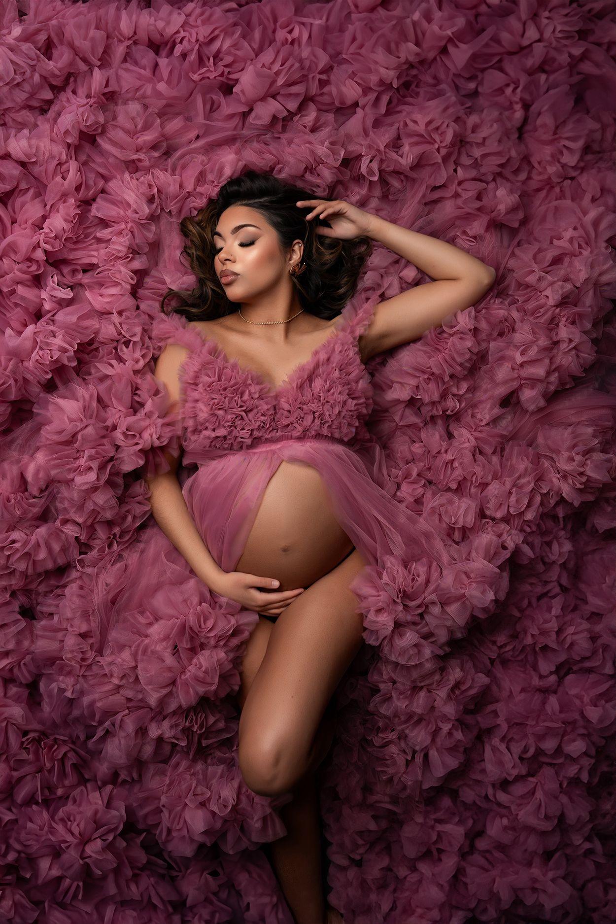 Artistic maternity photo with flowing pink tulle fabric and ruffles creating a dreamy backdrop.