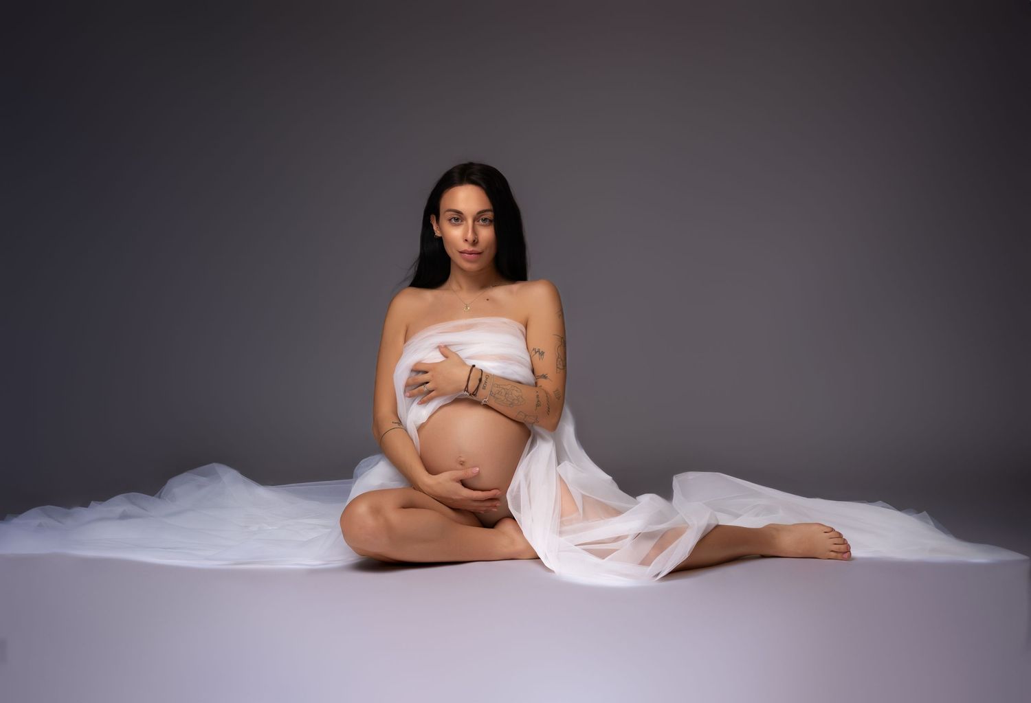Artistic black and white maternity photos showing an expectant mother in various elegant poses against a dark backdrop.