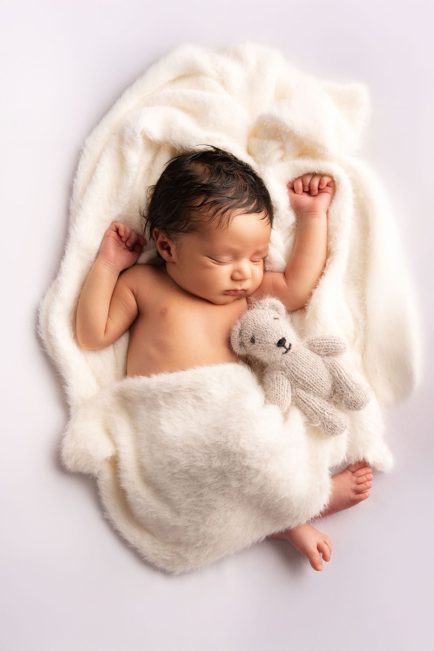 A sleeping newborn in white swaddle blankets lies with a small plush teddy bear across multiple frames.