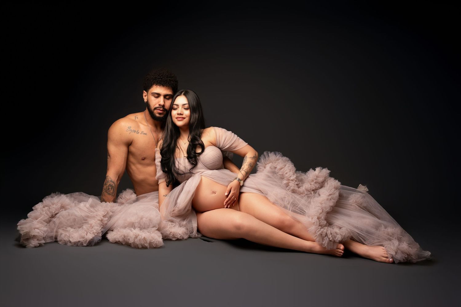 A side-lying figure is posed with flowing pink tulle fabric in a dramatic dark studio setting with artistic lighting.