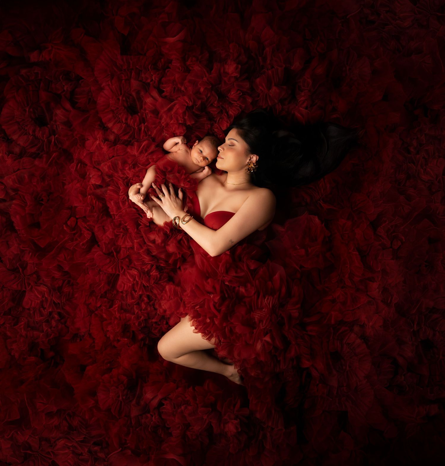Artistic portrait series with red floral backdrop showing tender moments between parent and infant in dramatic lighting.