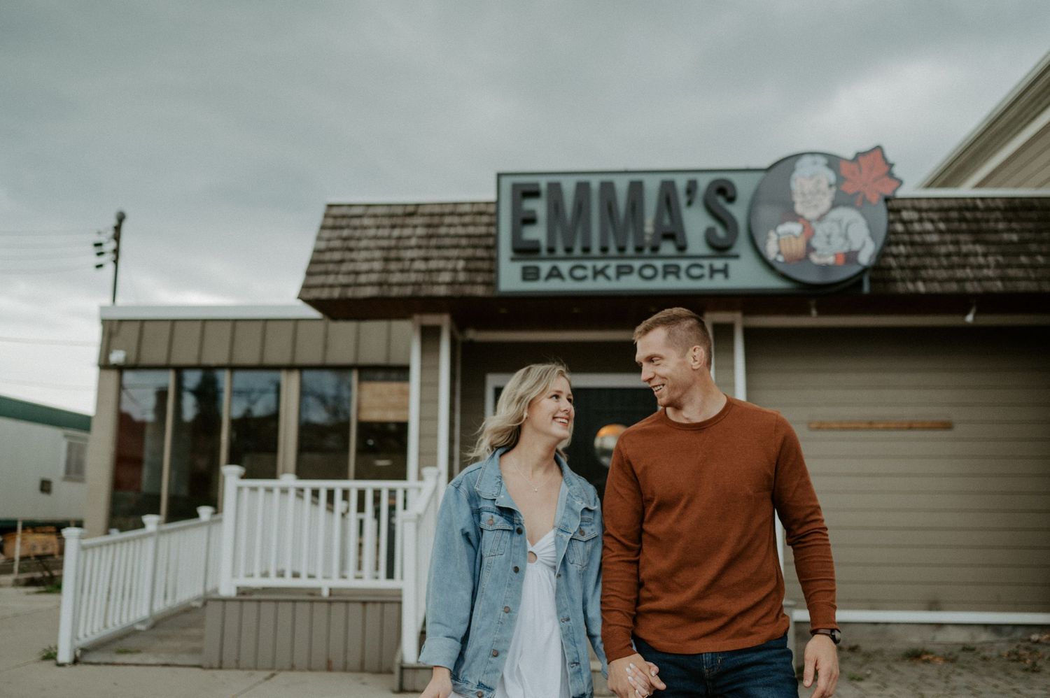 A couple walks together outside Emma's restaurant with a storefront sign visible under an overcast sky.