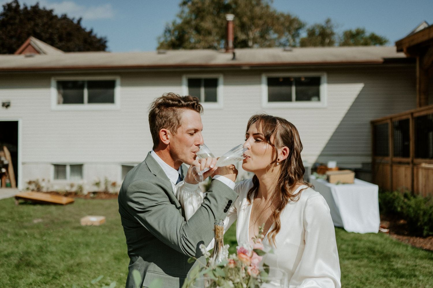 A couple shares a tender moment in a backyard with a white house and green lawn in the background.