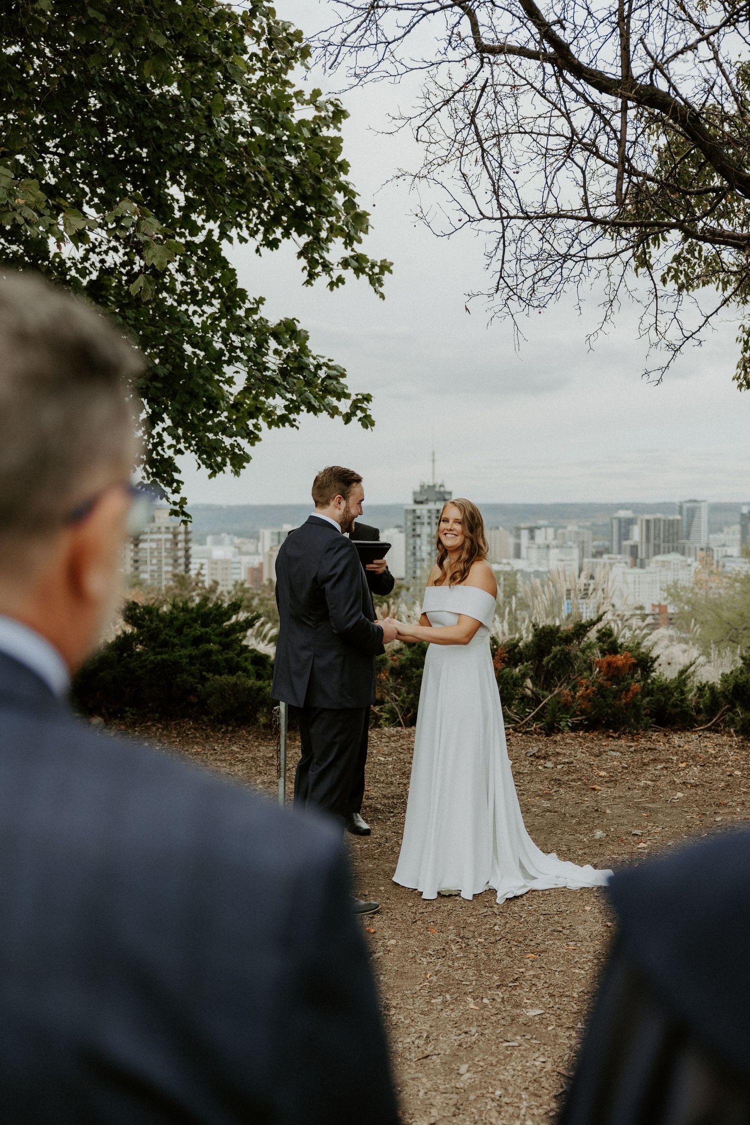 A loving couple shares a private wedding moment overlooking the city skyline while groomsmen watch from behind.