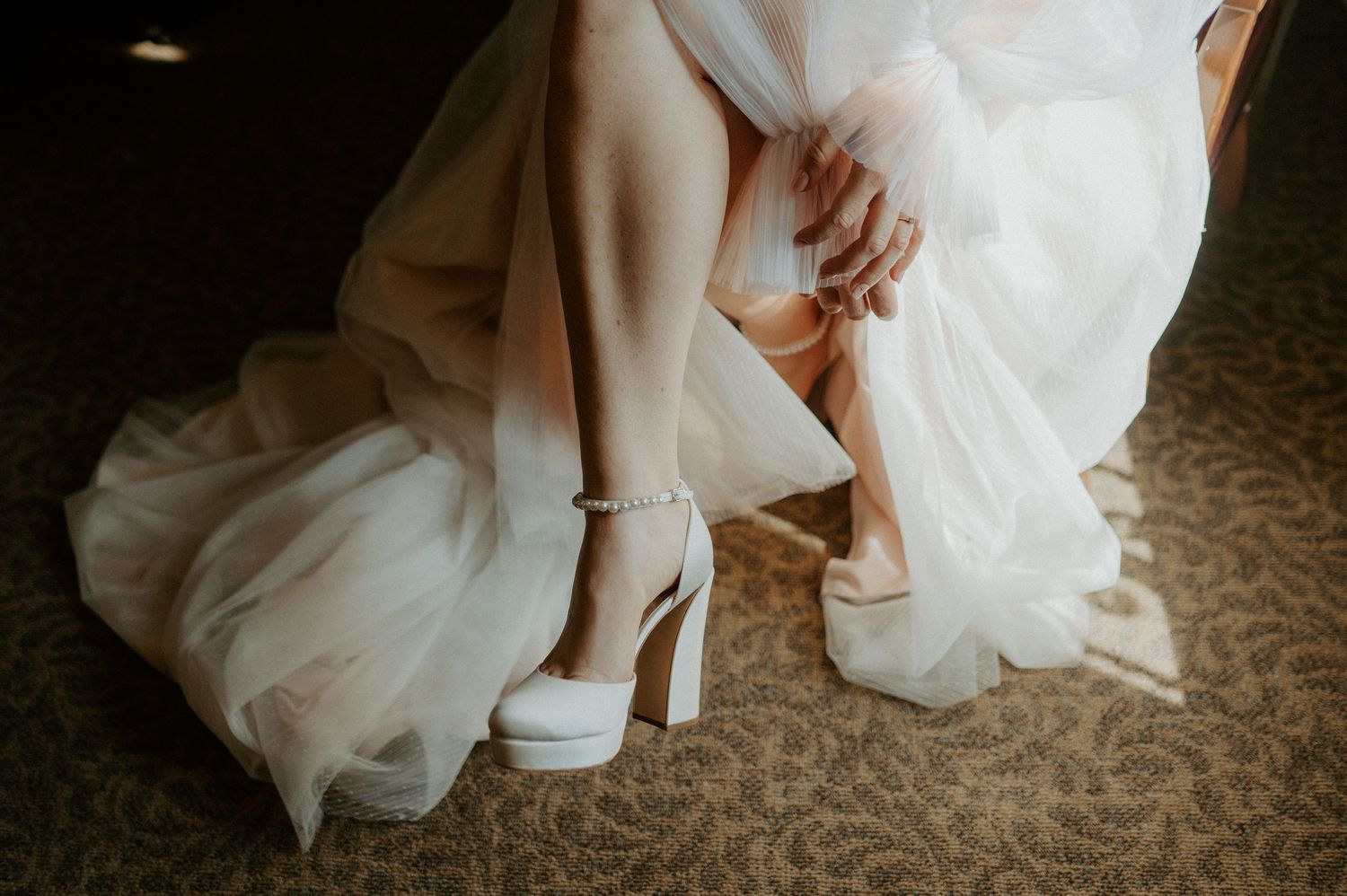 Close-up view of a bride adjusting her white platform heels while wearing a flowing wedding dress.