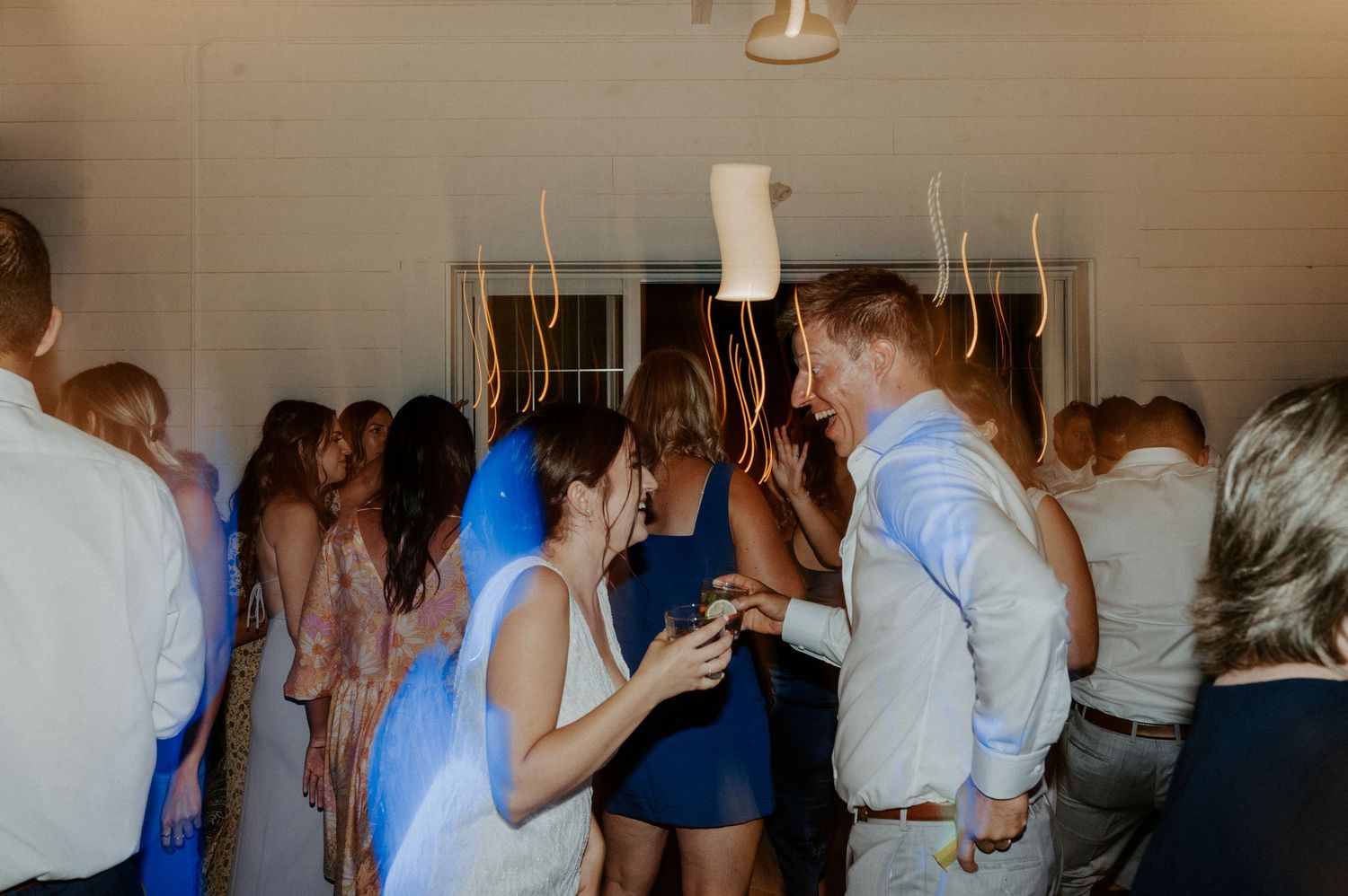 Party guests dancing and celebrating on a crowded dance floor at an indoor event with ambient lighting.