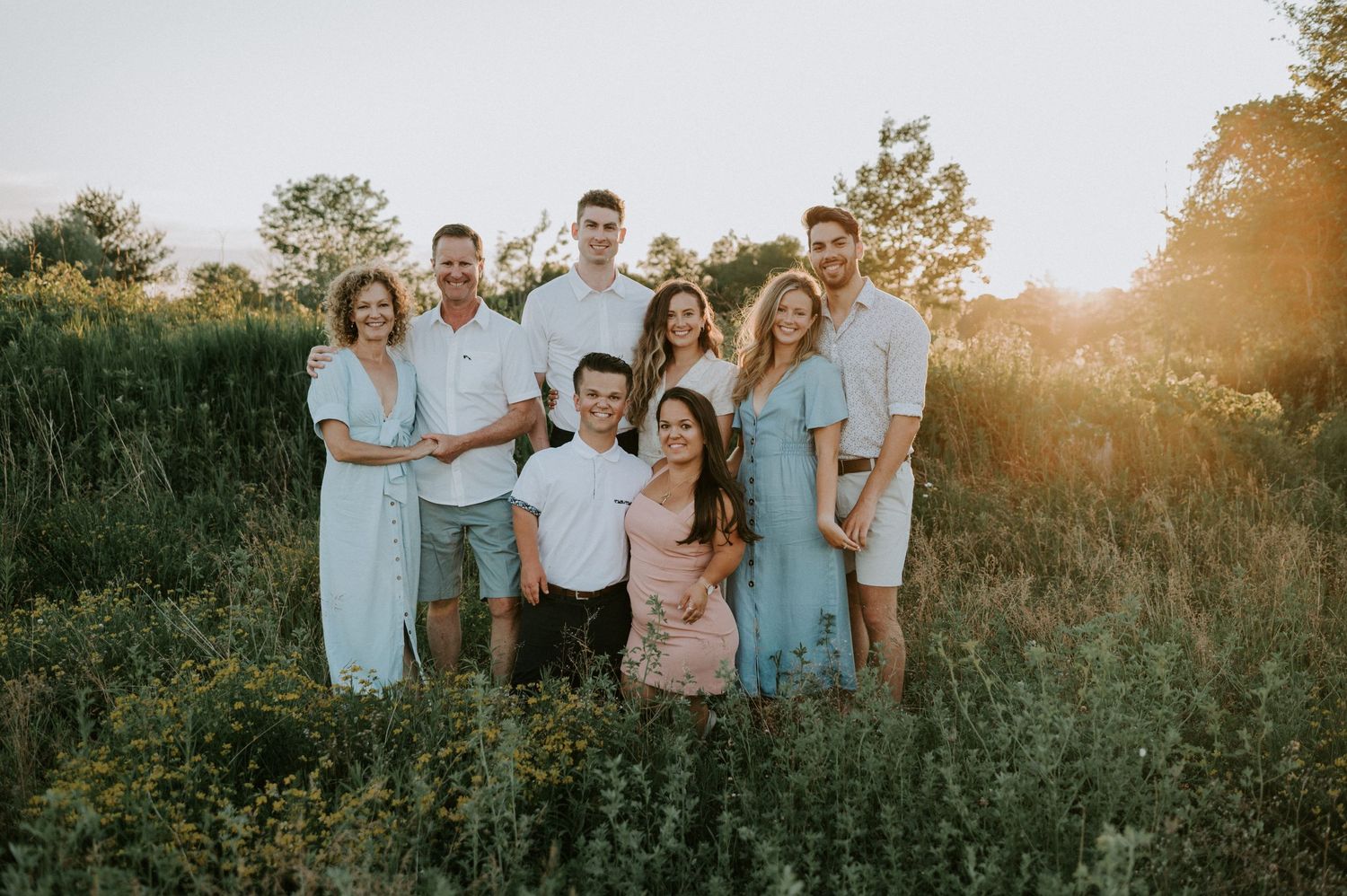 A family photoshoot with everyone posing together in a sunlit meadow during golden hour.