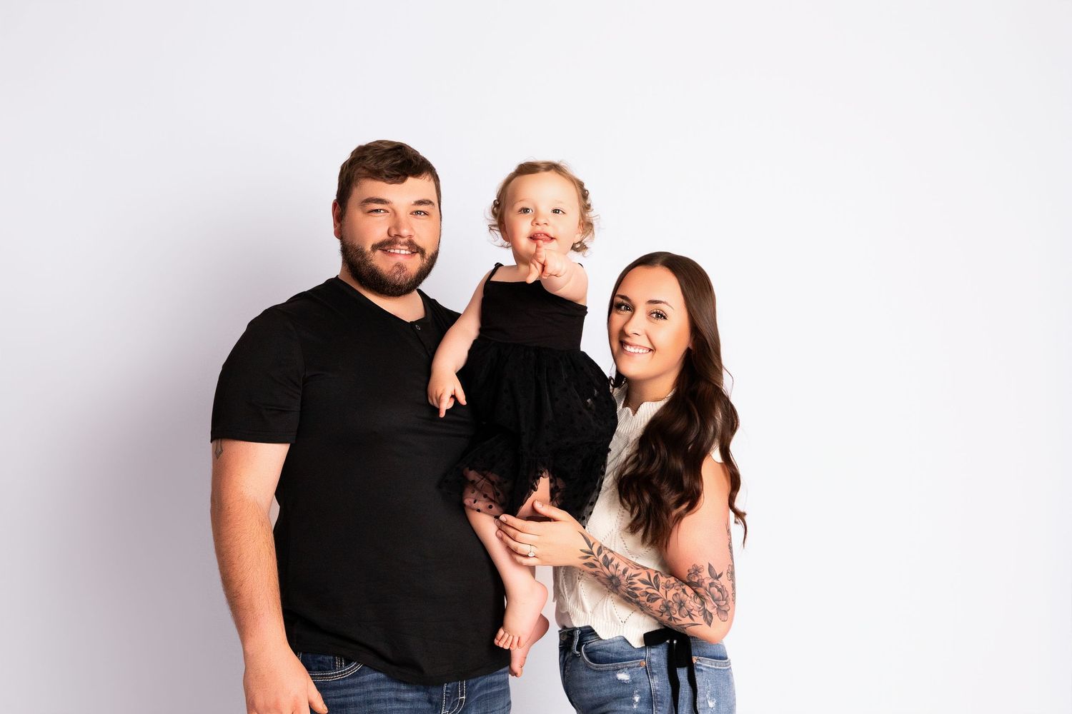 A family in black and white outfits poses together against a white background in a studio setting.