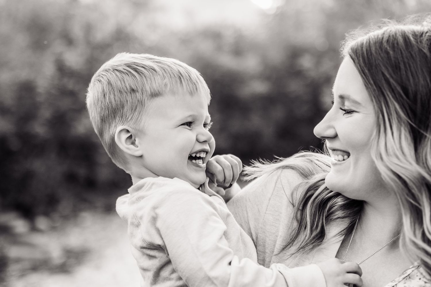Black and white photo of a laughing toddler boy being held by a smiling young woman outdoors.