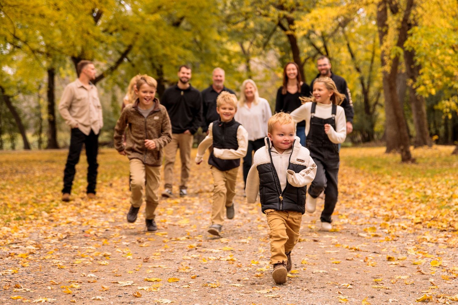 A group running and playing together through fallen autumn leaves in a park.