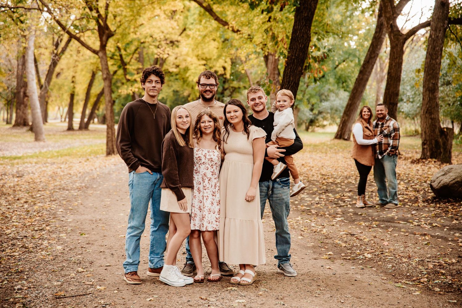 Extended family group poses together on a tree-lined path with golden autumn leaves.